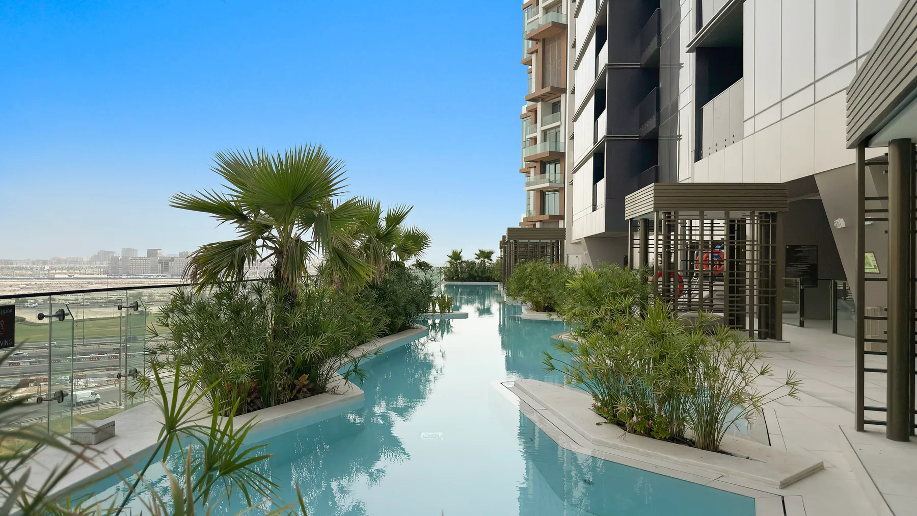 Una piscina al aire libre junto a un edificio moderno, con palmeras y plantas.