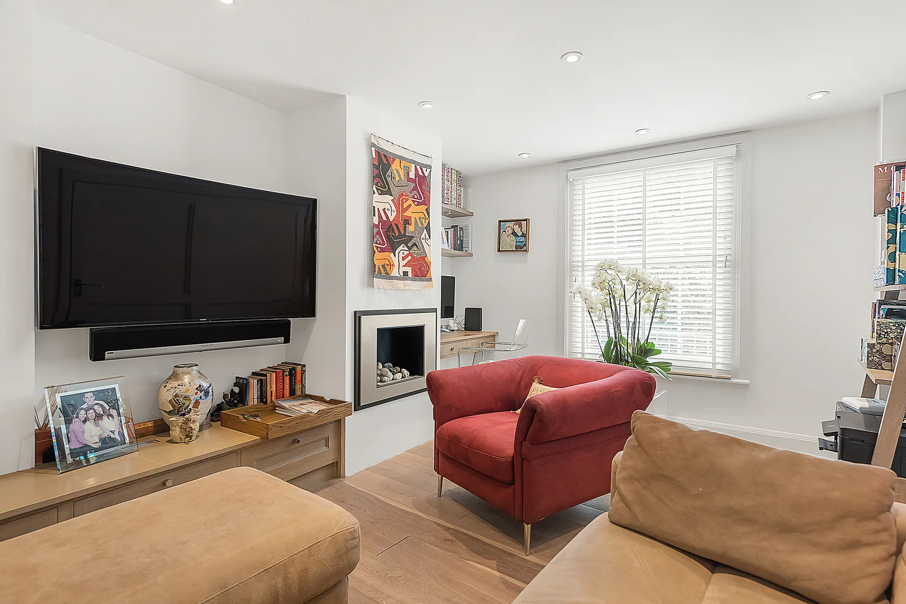 Una sala luminosa con un sofá rojo, un televisor y ventanas grandes.