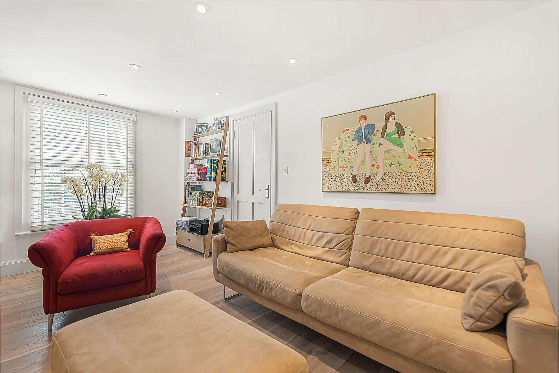 Una sala de estar luminosa con asientos, una ventana amplia y una obra enmarcada.