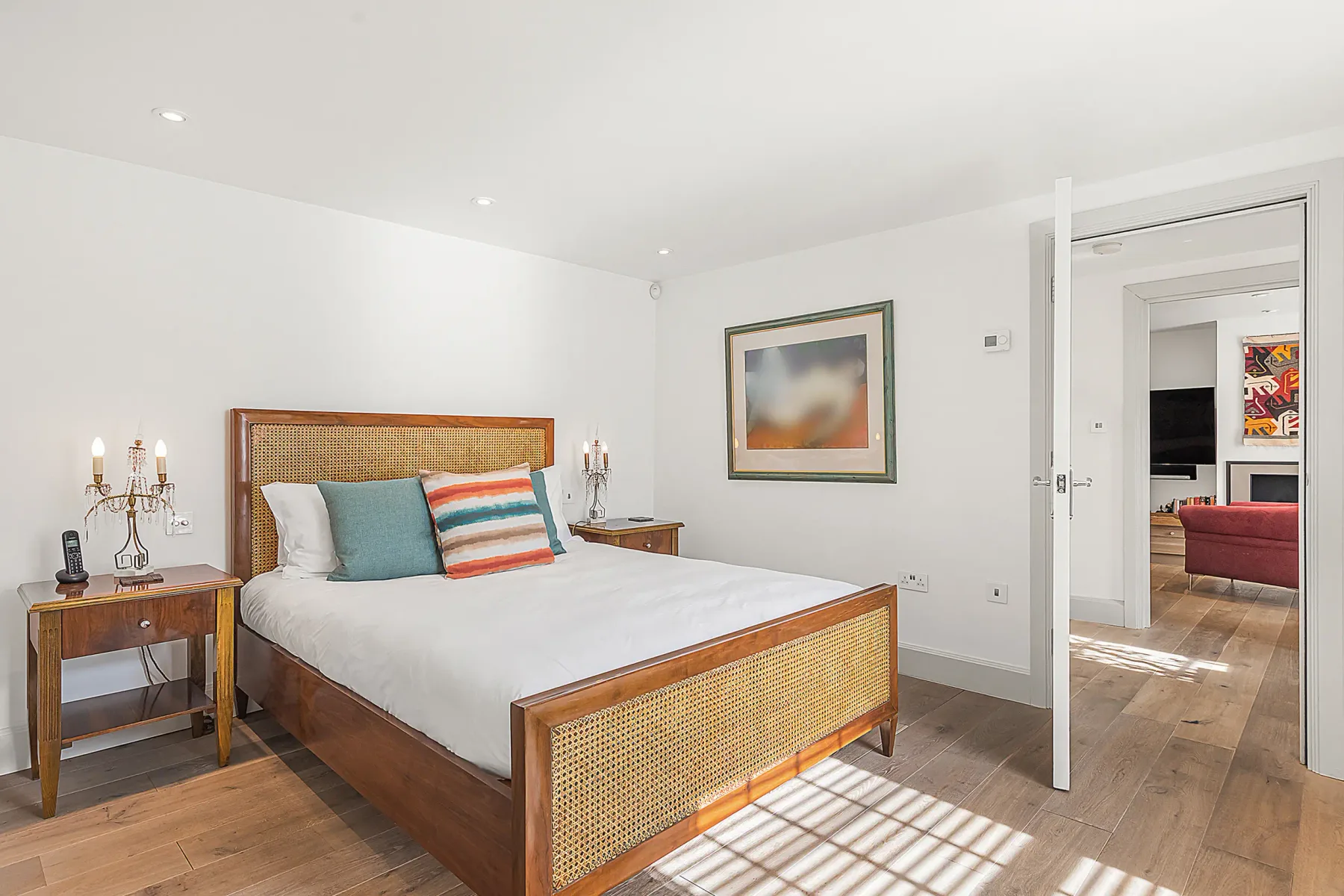 Un dormitorio luminoso con una cama, mesitas de noche y una puerta abierta.