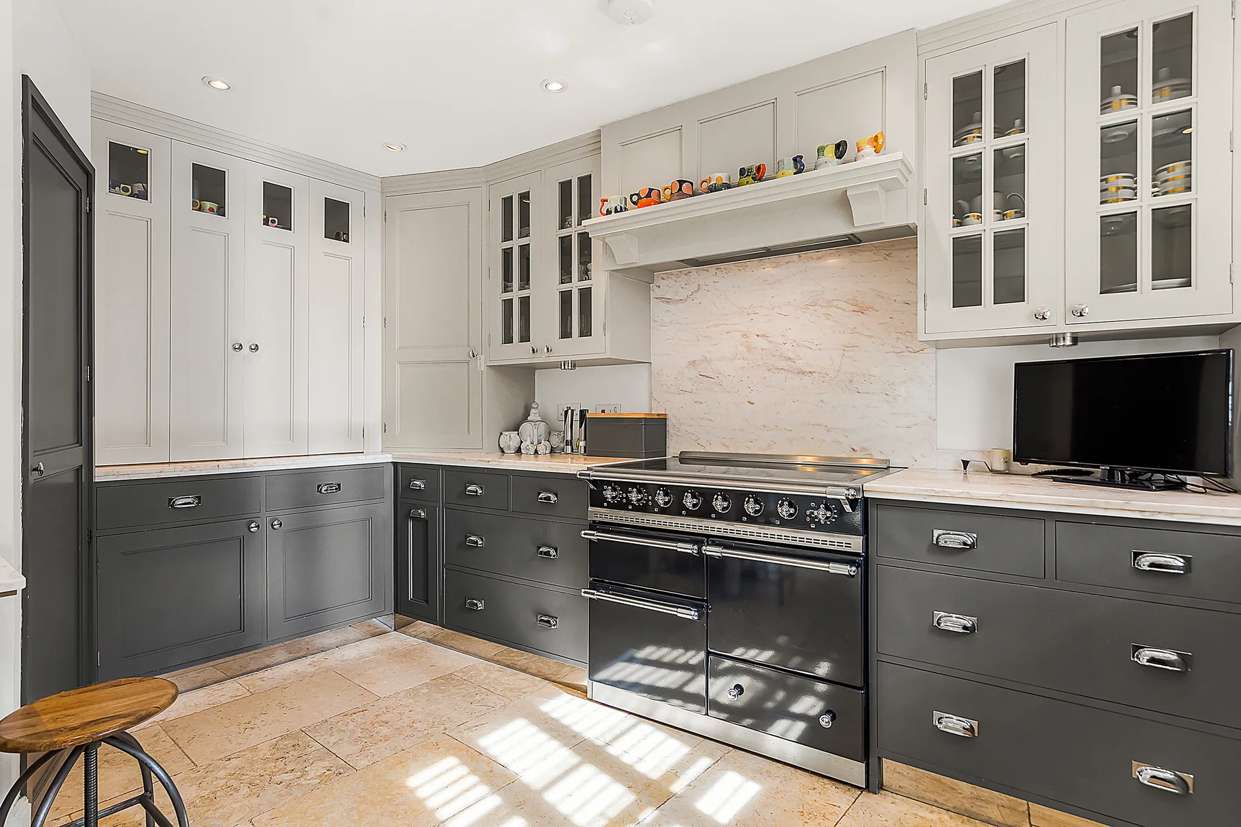 A spacious kitchen with gray cabinetry, a central range, and a light stone backsplash.