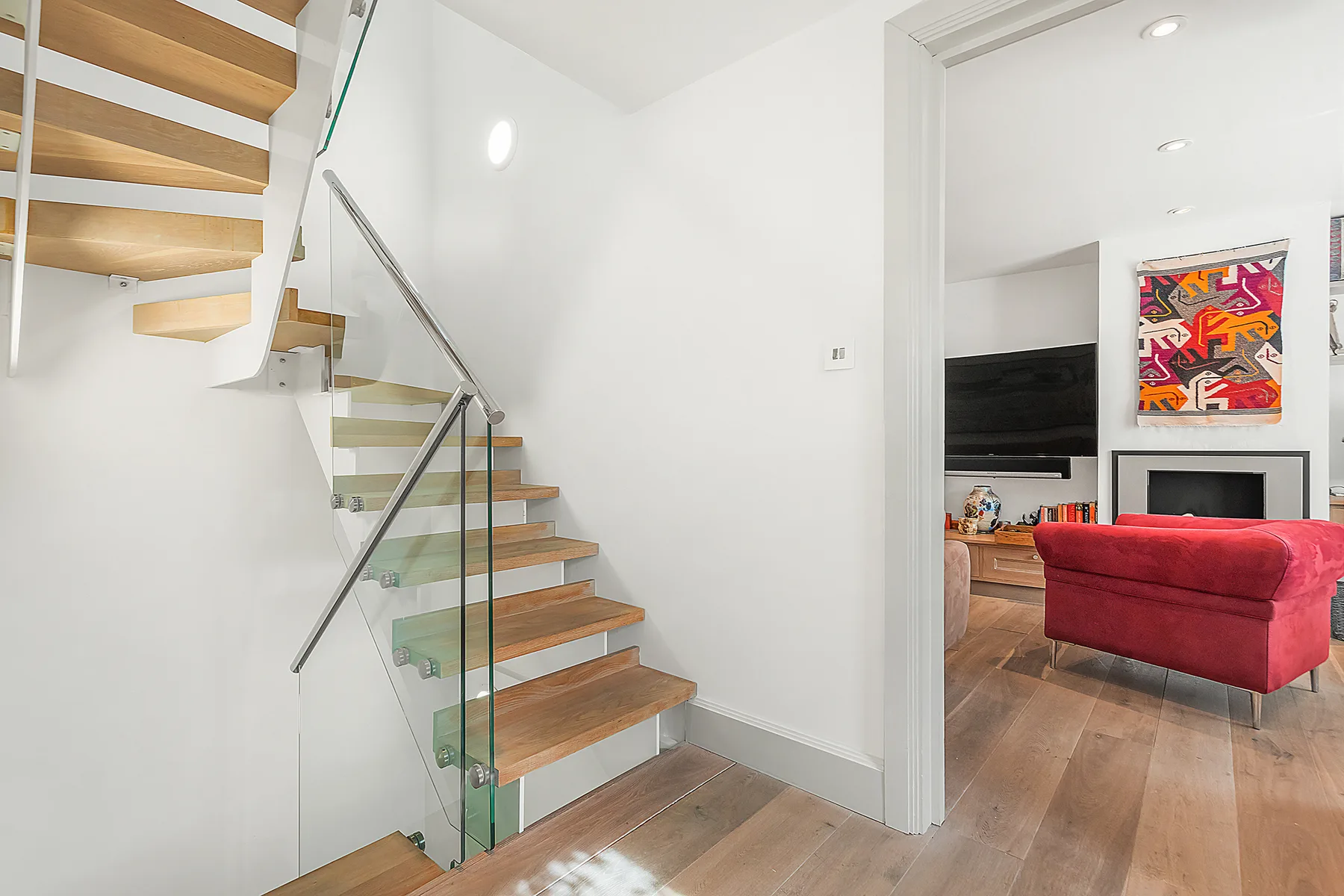 Una escalera con peldaños de madera y barandilla de vidrio da a una sala de estar.