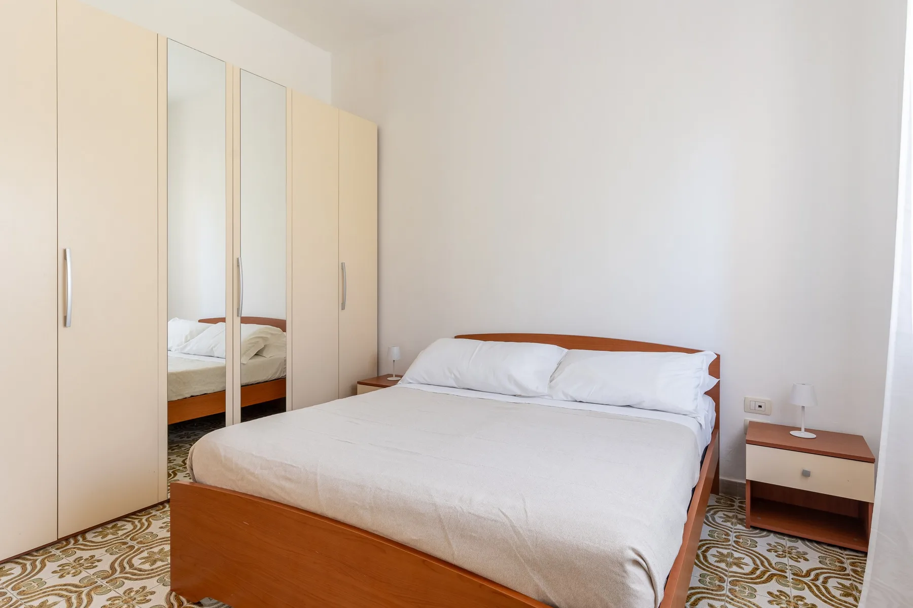 Un dormitorio luminoso con una cama doble y un armario con espejo.