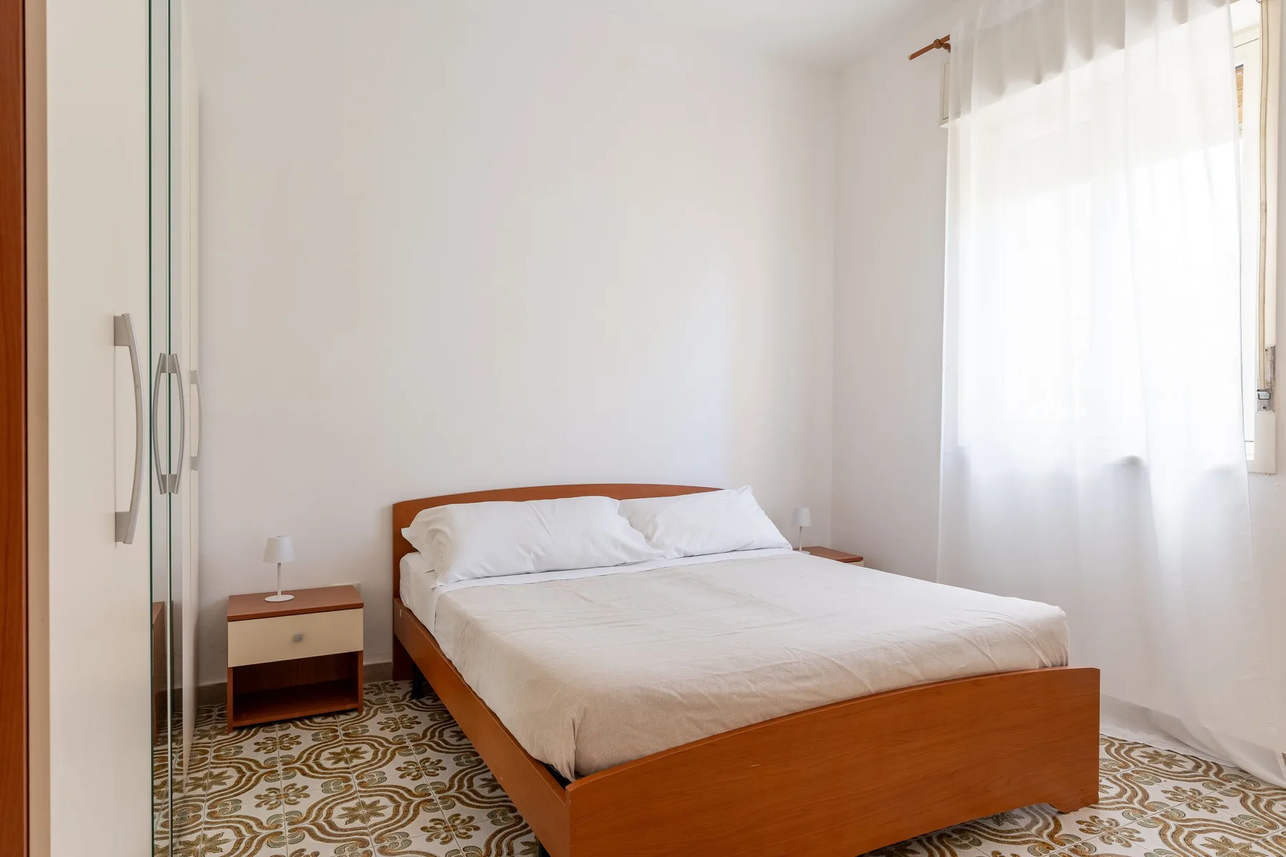 Un dormitorio luminoso con una cama de madera y una gran ventana con cortinas.