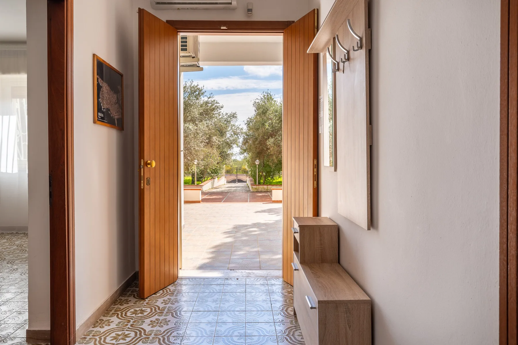 Una entrada se abre a través de puertas de madera hacia una terraza soleada.