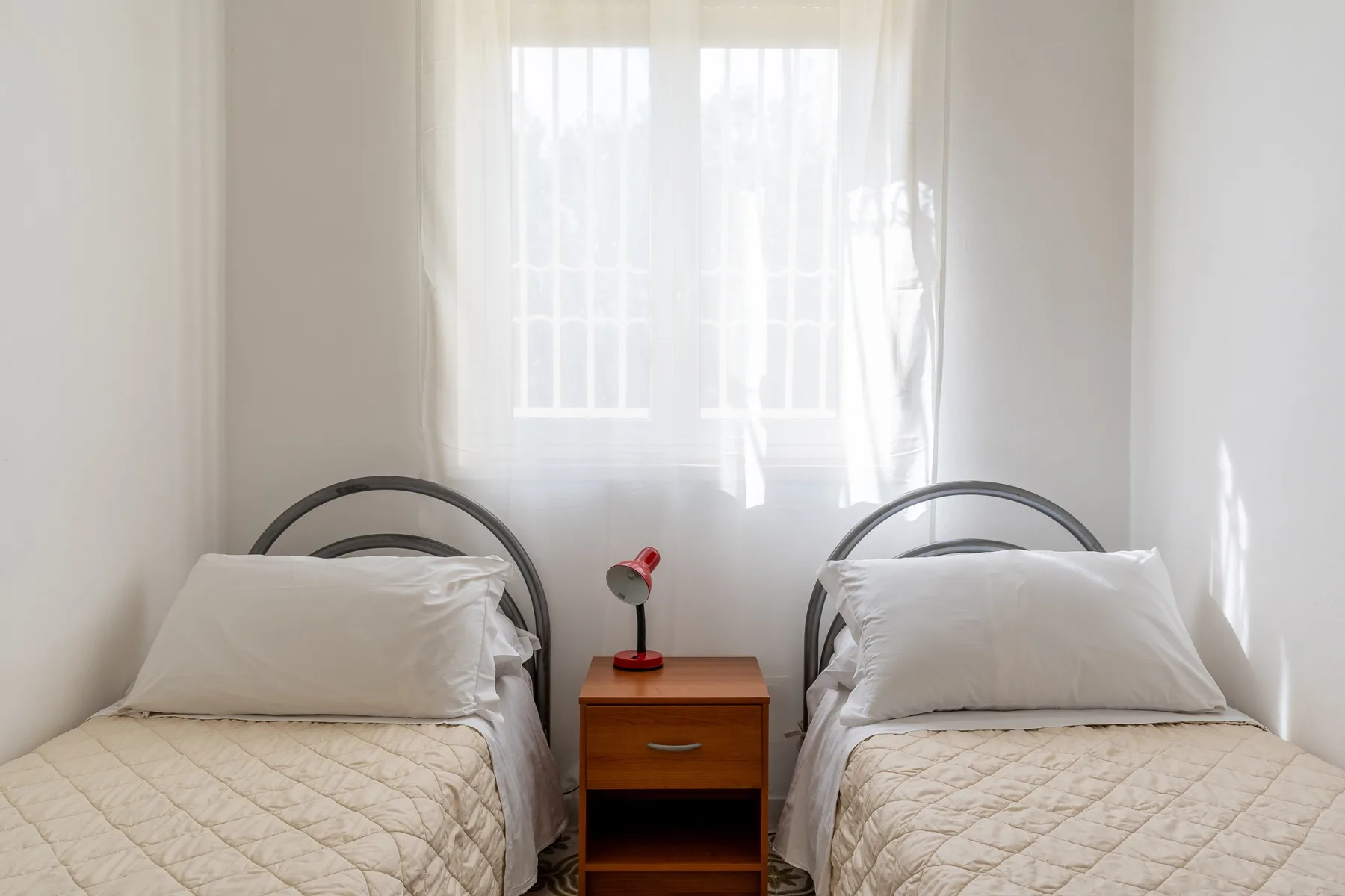 Un dormitorio luminoso con dos camas individuales y una pequeña mesa de noche.