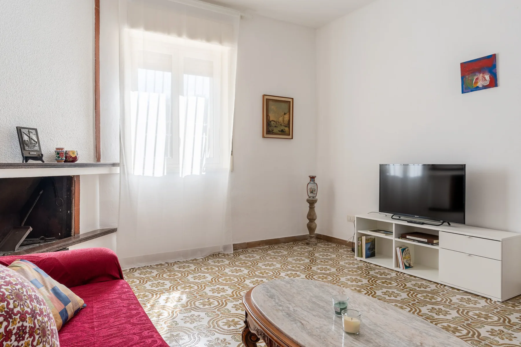 Una sala de estar con televisor, asientos rojos y suelo estampado.