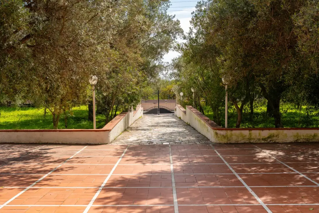 Un camino pavimentado atraviesa un jardín arbolado hacia una puerta cerrada.
