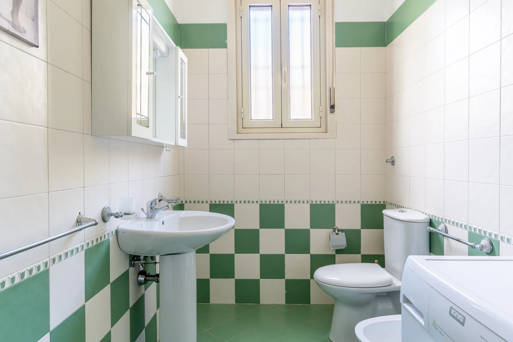 Un baño alicatado con lavabo, inodoro y detalles verdes y blancos en las paredes.