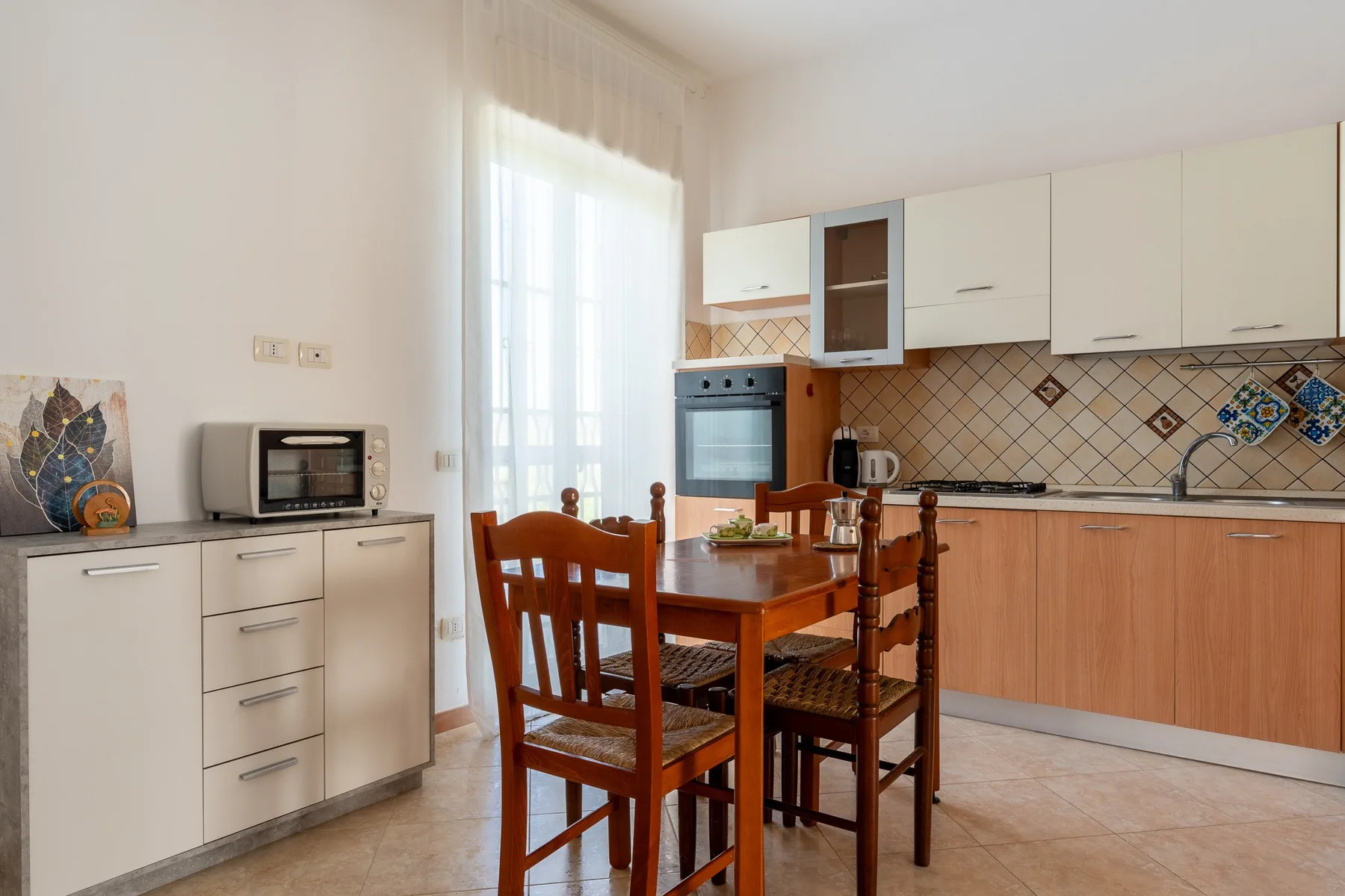 Una cocina luminosa con asientos de madera junto a armarios blancos y un salpicadero de azulejos.