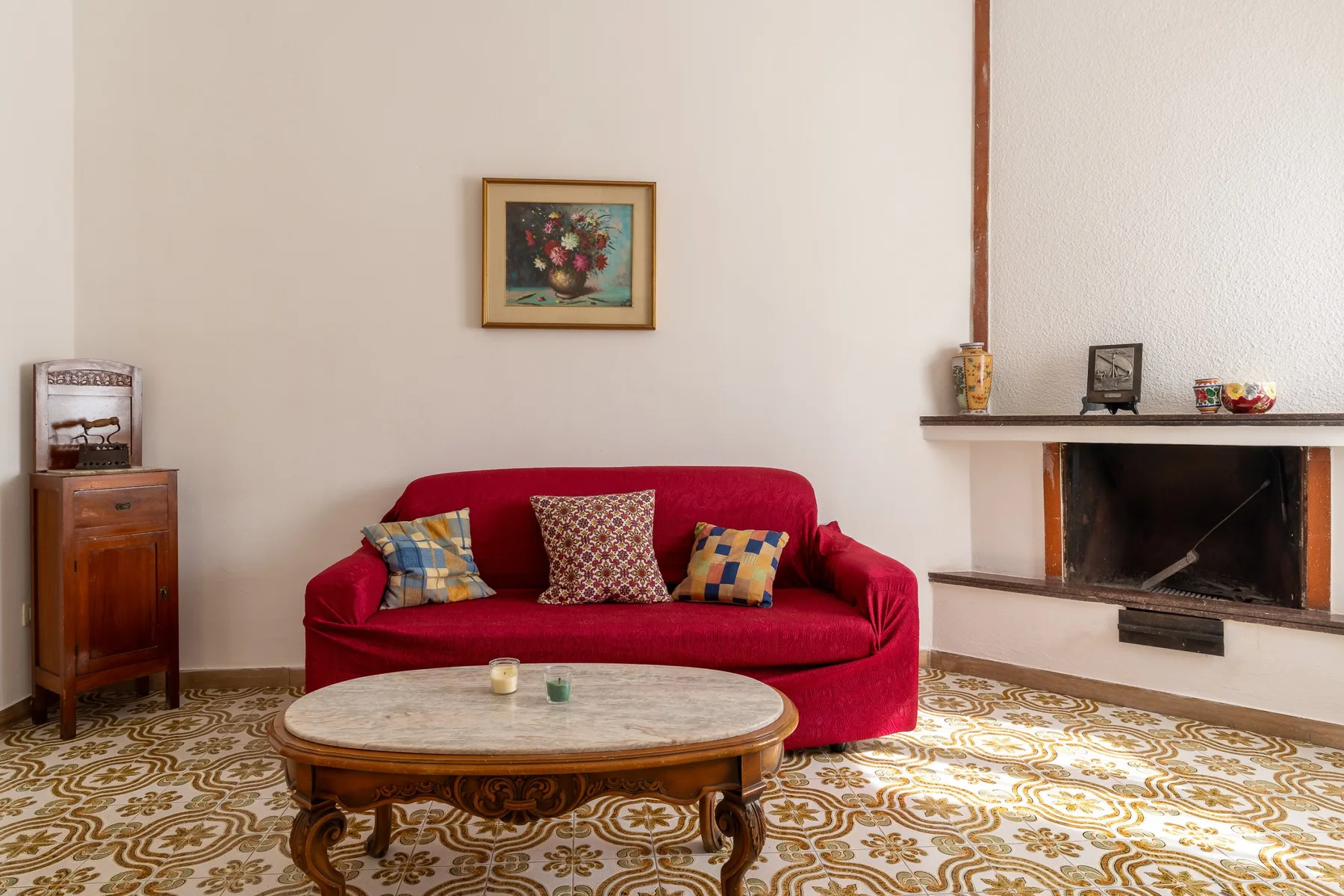 Una sala de estar con un sofá rojo, suelo estampado y chimenea.