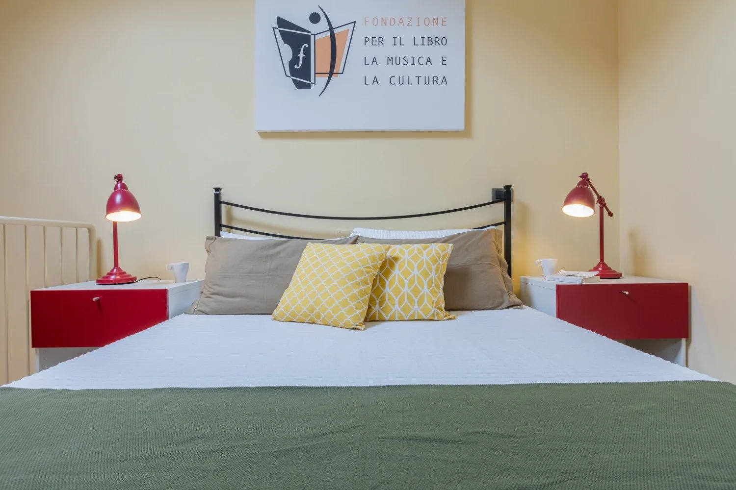 Un dormitorio con una cama bien tendida y mesitas de noche rojas a juego.
