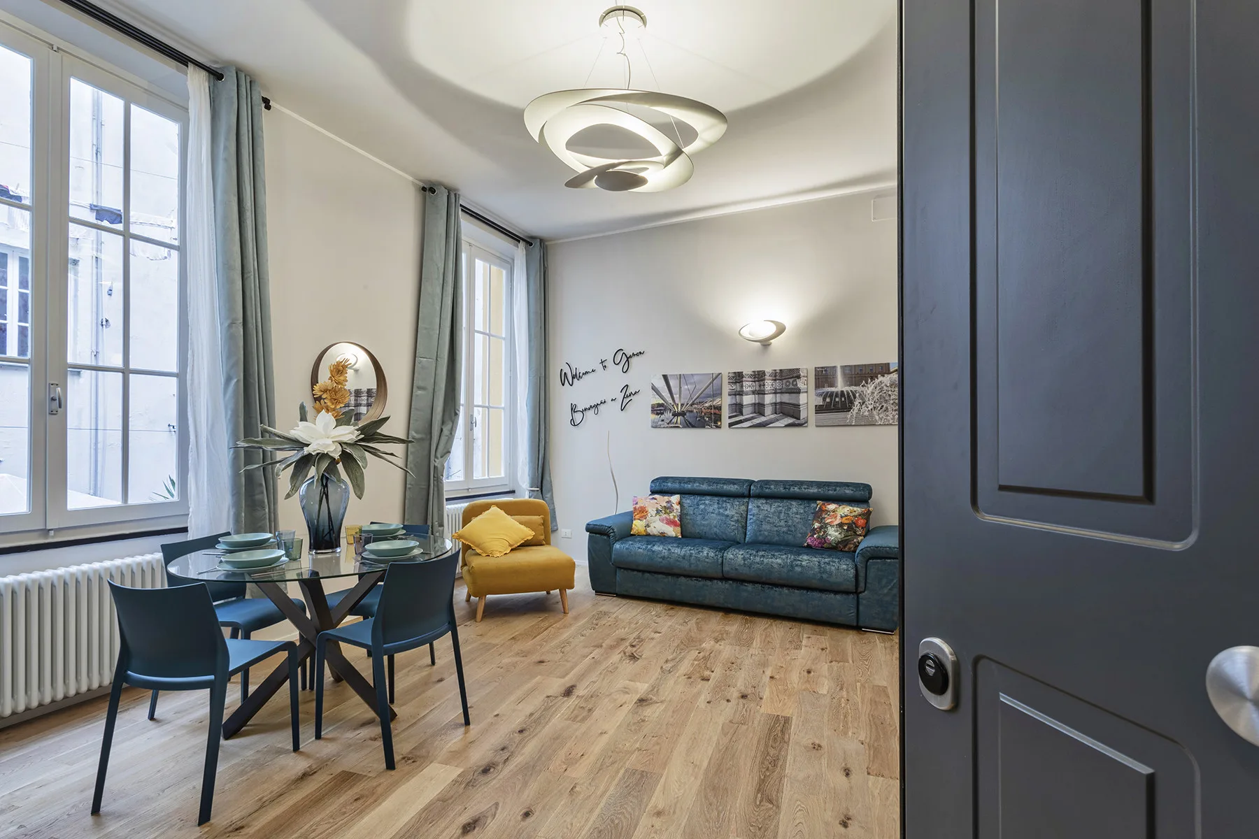 Una sala de estar con un sofá azul, una mesa pequeña y ventanas altas.
