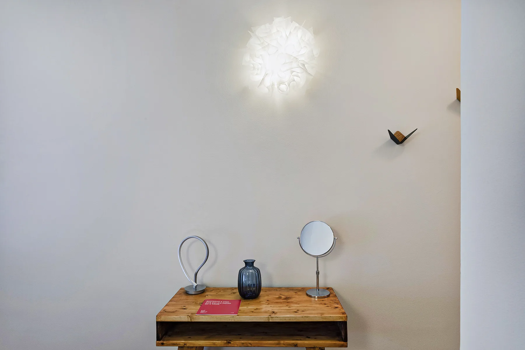 Una pequeña mesa de madera está junto a una pared clara, debajo de una lámpara brillante.