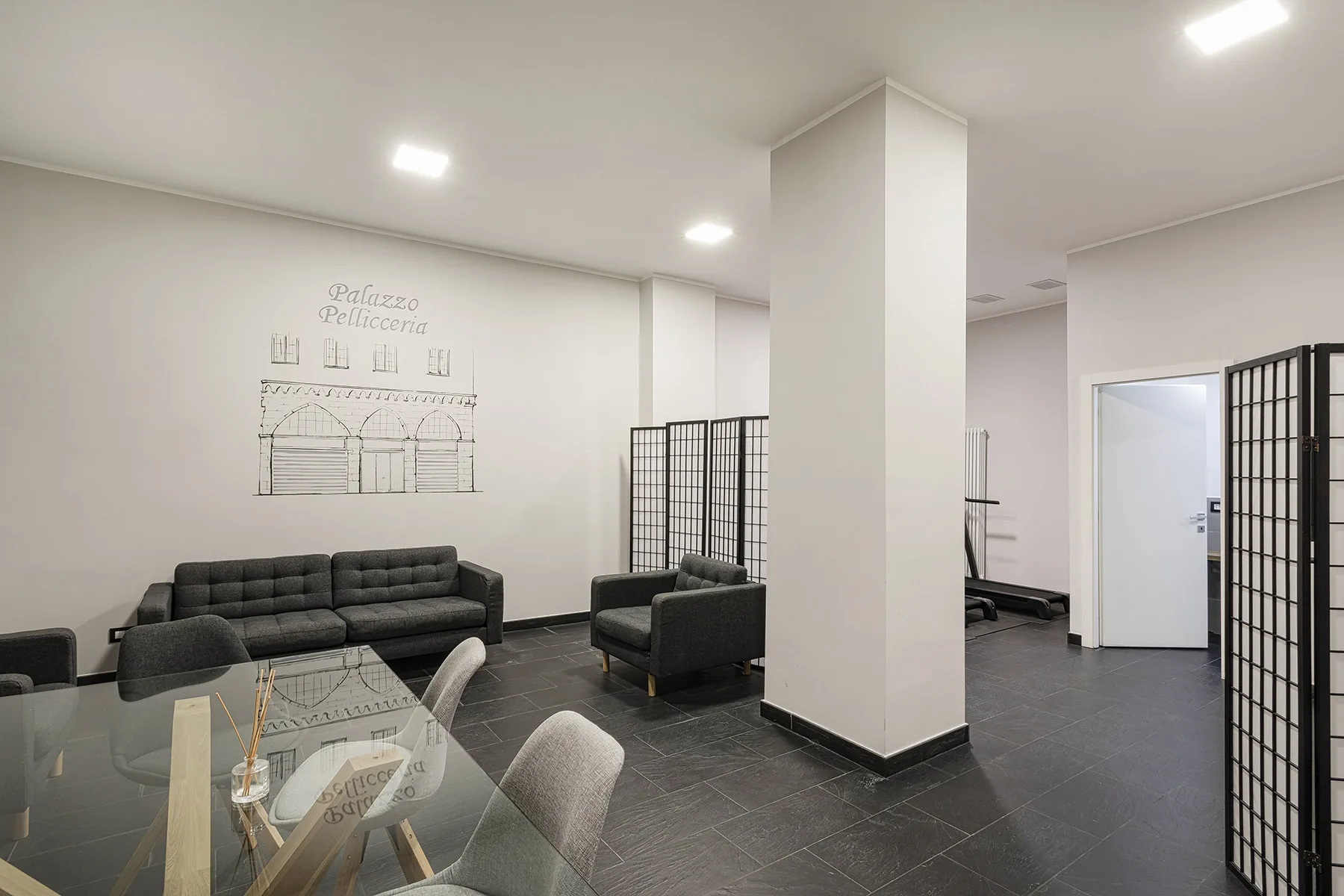 Una sala moderna con asientos oscuros, una mesa de vidrio y biombos plegables.