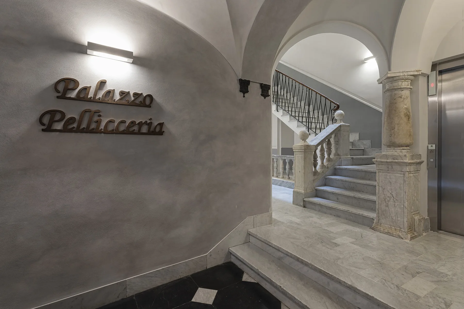 Una escalera interior con arco, peldaños de piedra y una barandilla decorativa.
