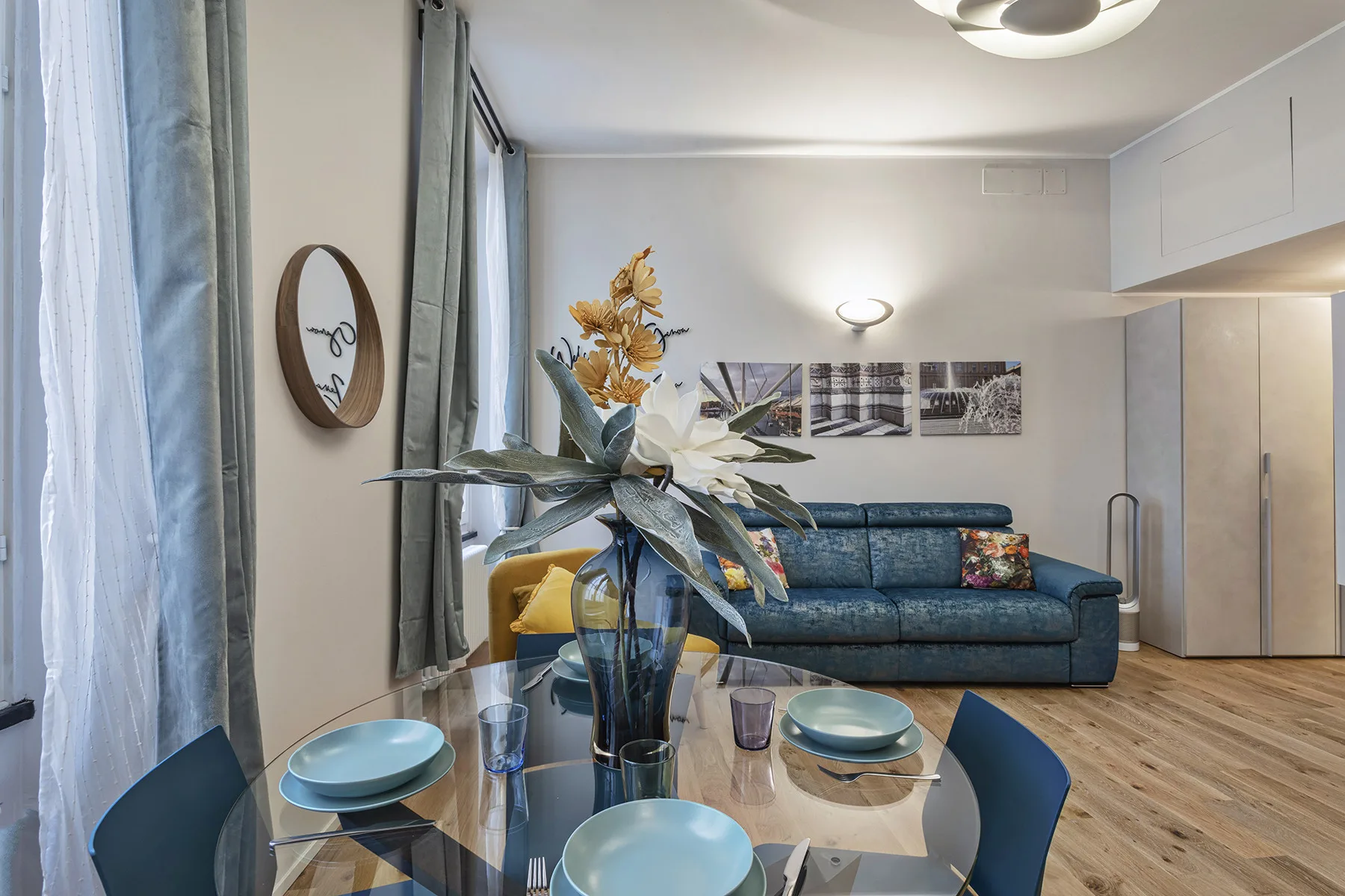 Comedor con una mesa de vidrio y asientos azules junto a un sofá.