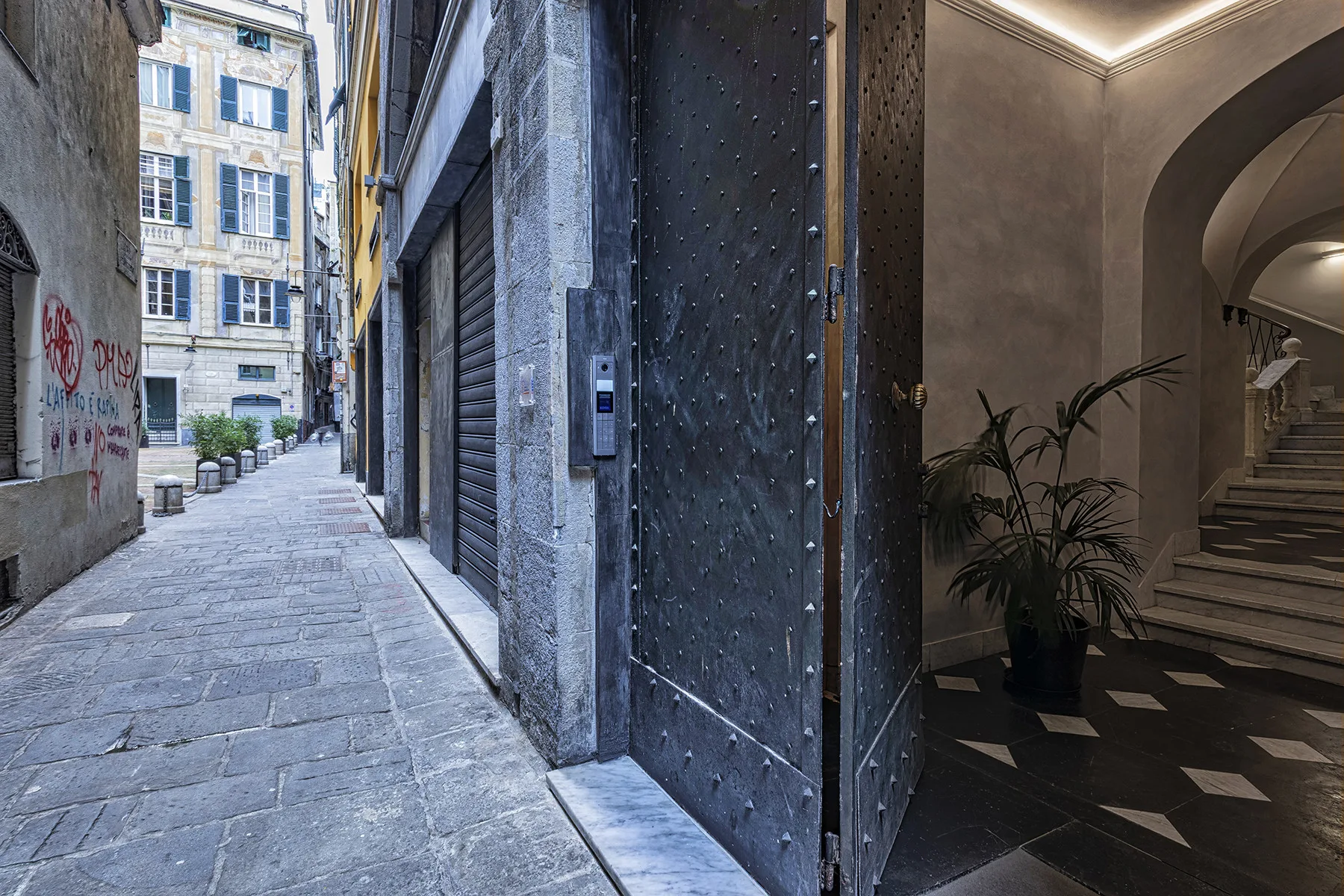 Un callejón estrecho con pavimento de piedra junto a una entrada oscura y una escalera interior visible.
