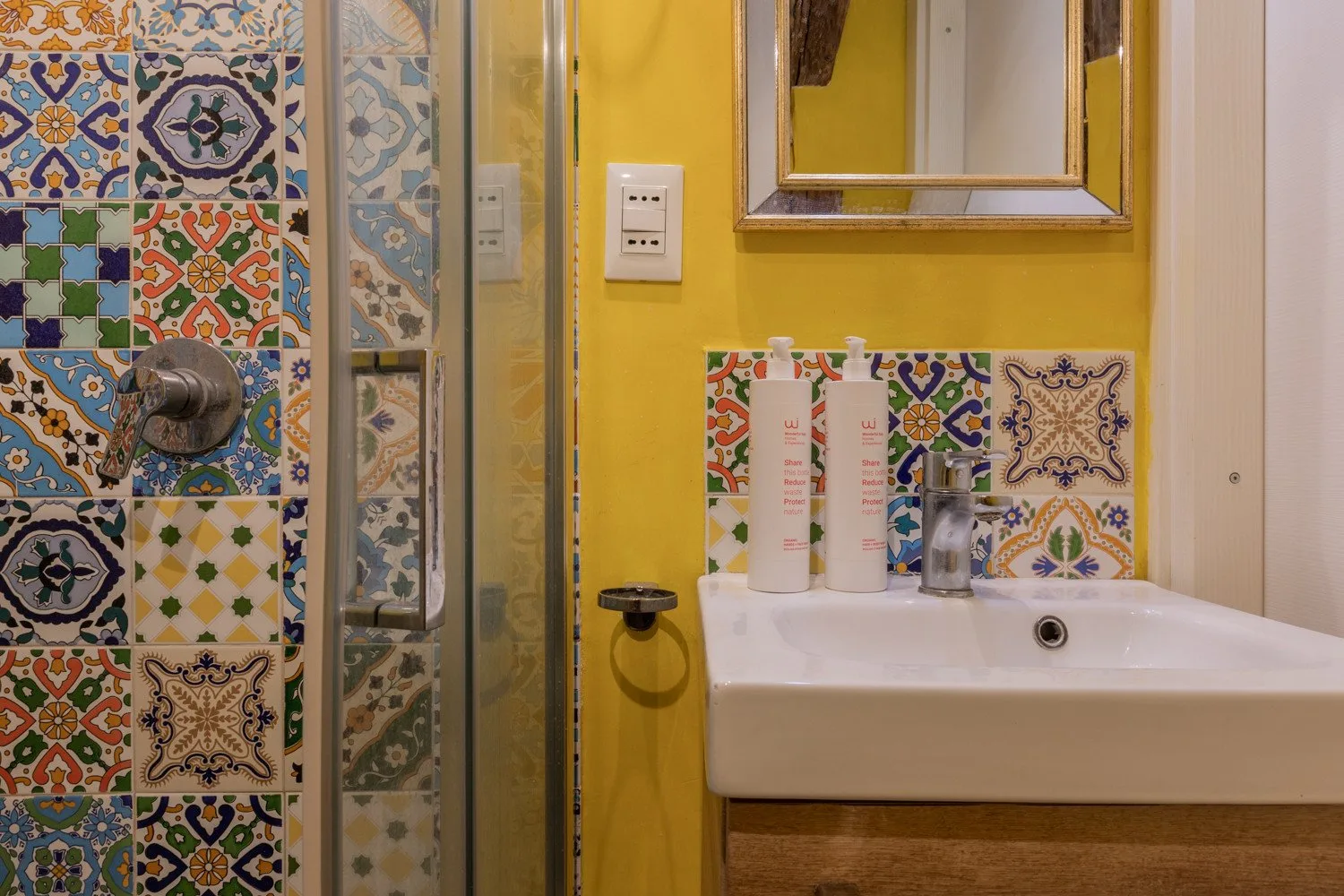 A colorful bathroom with a patterned tile wall and a white sink.