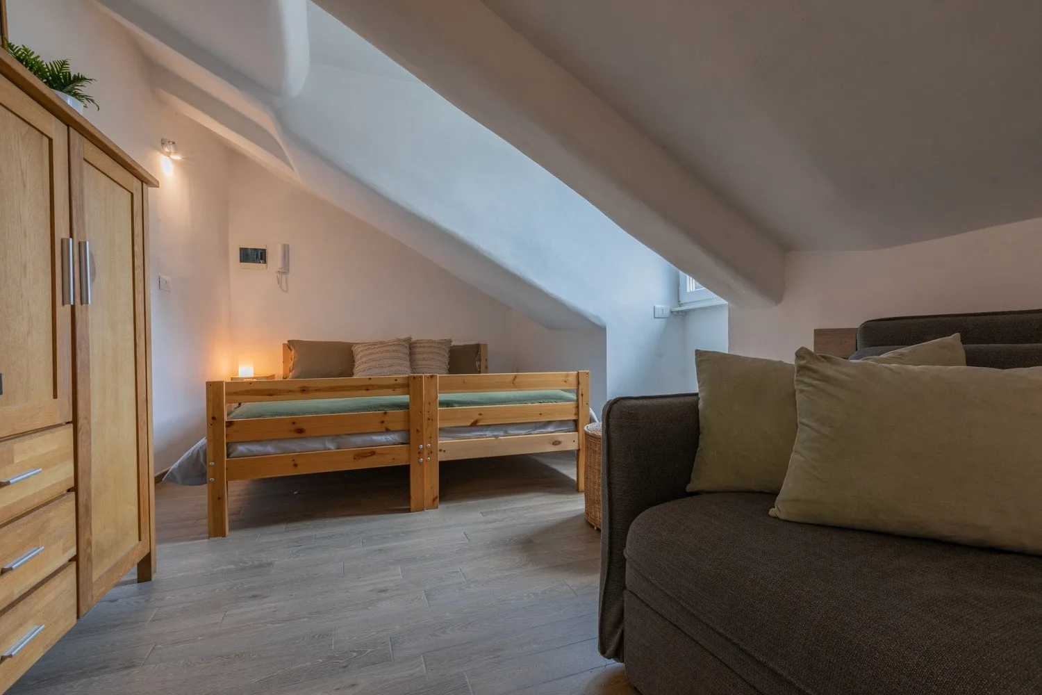An attic bedroom with a wooden bed and a dark sofa.