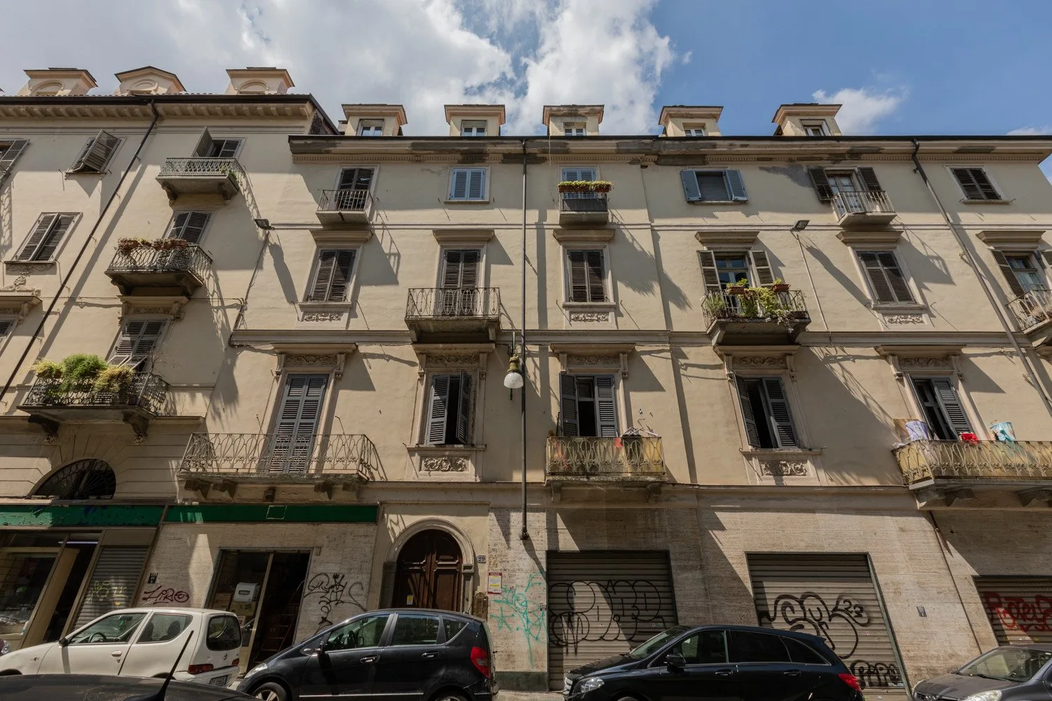 A multi-story building facade with balconies and shuttered windows faces the street.