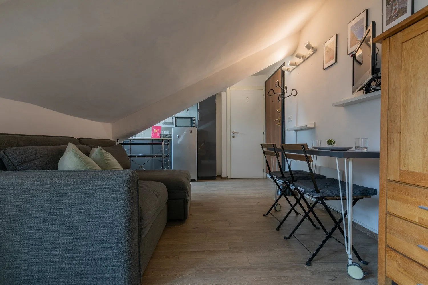 A compact living and dining area with a sofa beneath a sloped ceiling.