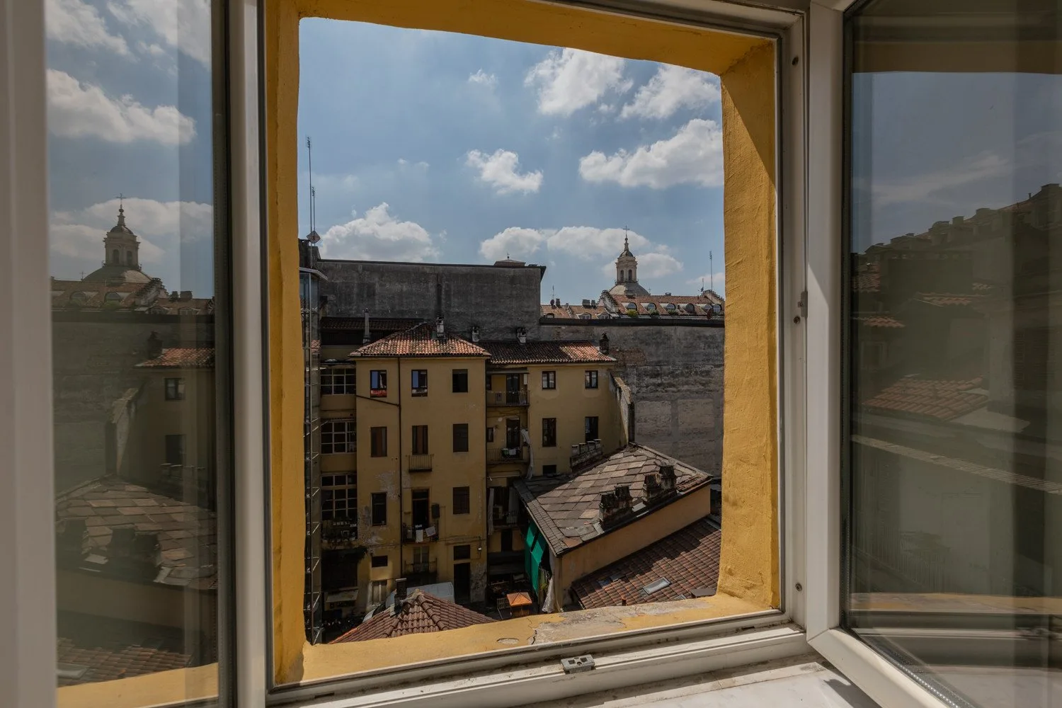 A city view through an open window, with rooftops and a cloudy sky.