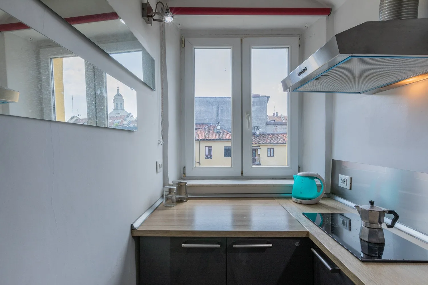A compact kitchen with a countertop, cooktop, and windows overlooking nearby buildings.