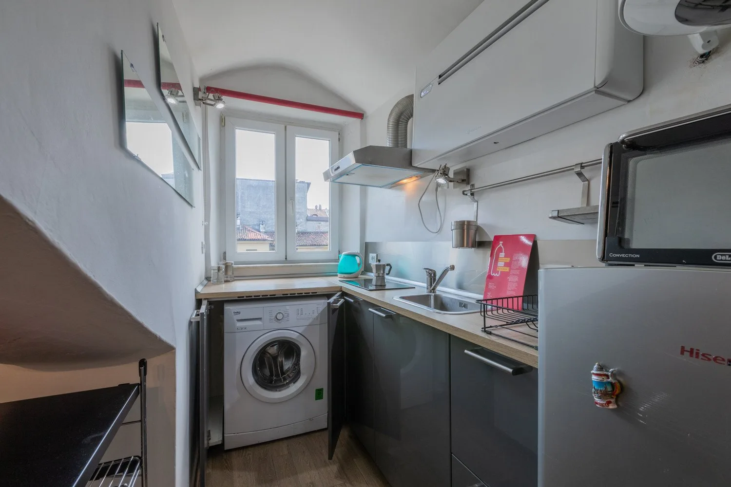 A compact kitchen with a washing machine beneath the counter and a window.