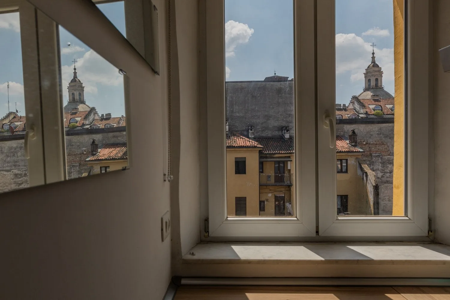 A room with tall windows overlooking tiled rooftops and a distant church tower.