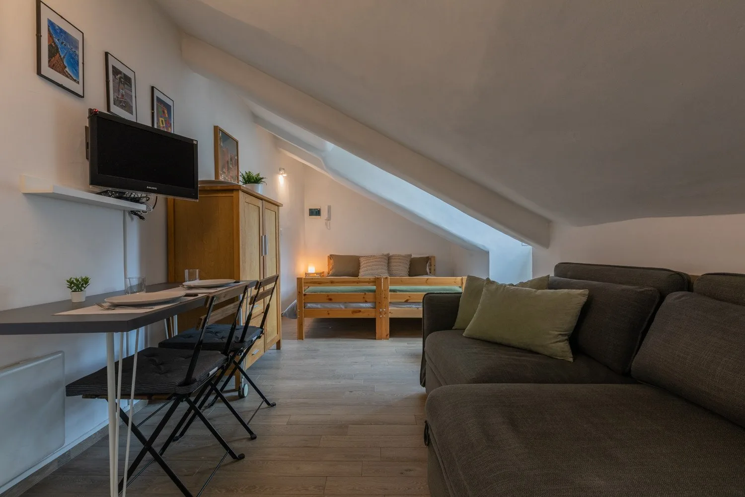 Una sala abuhardillada amueblada con mesa de comedor, asientos y un televisor.
