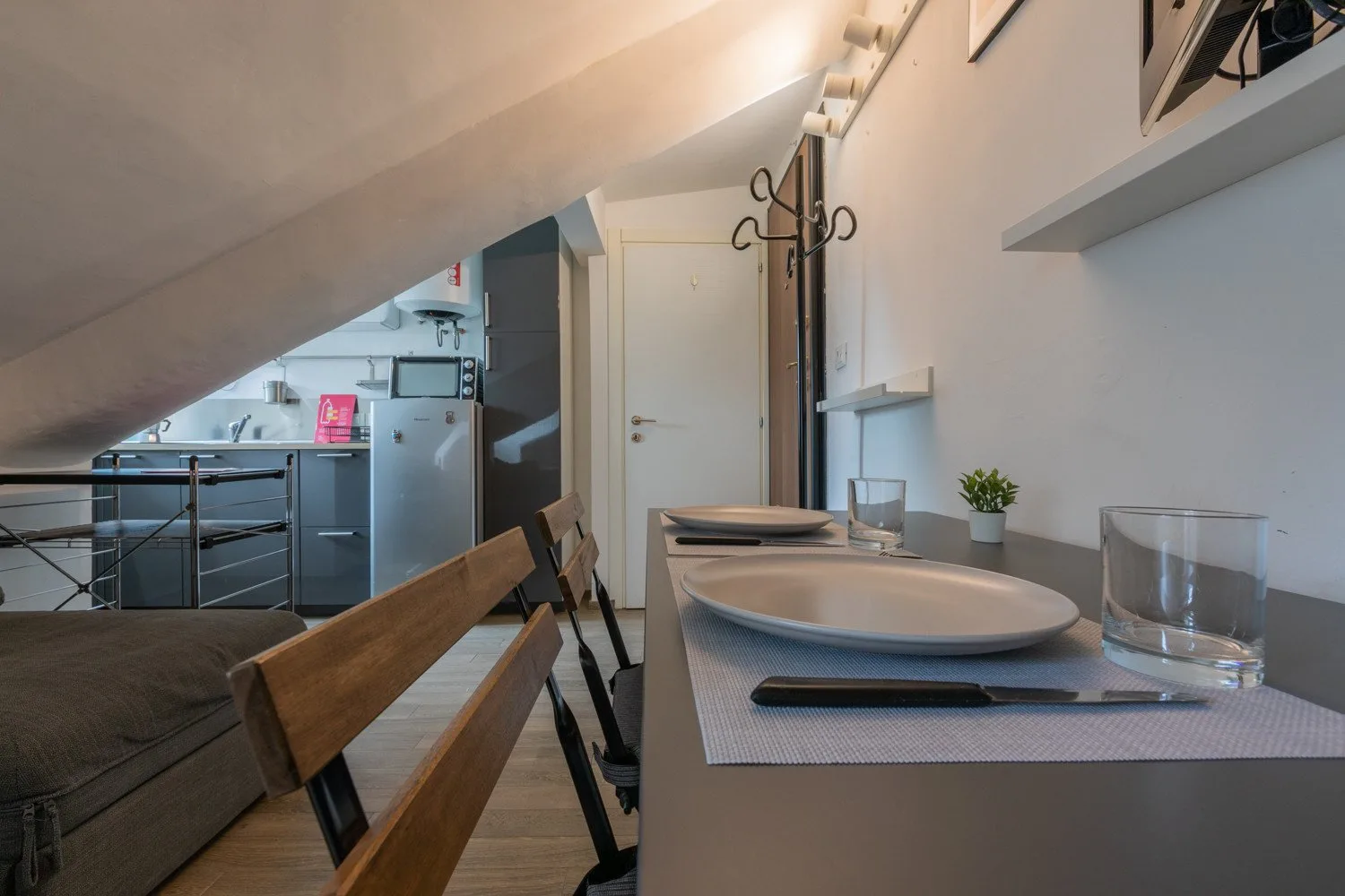 A dining area with place settings beside a compact kitchen under a sloped ceiling.