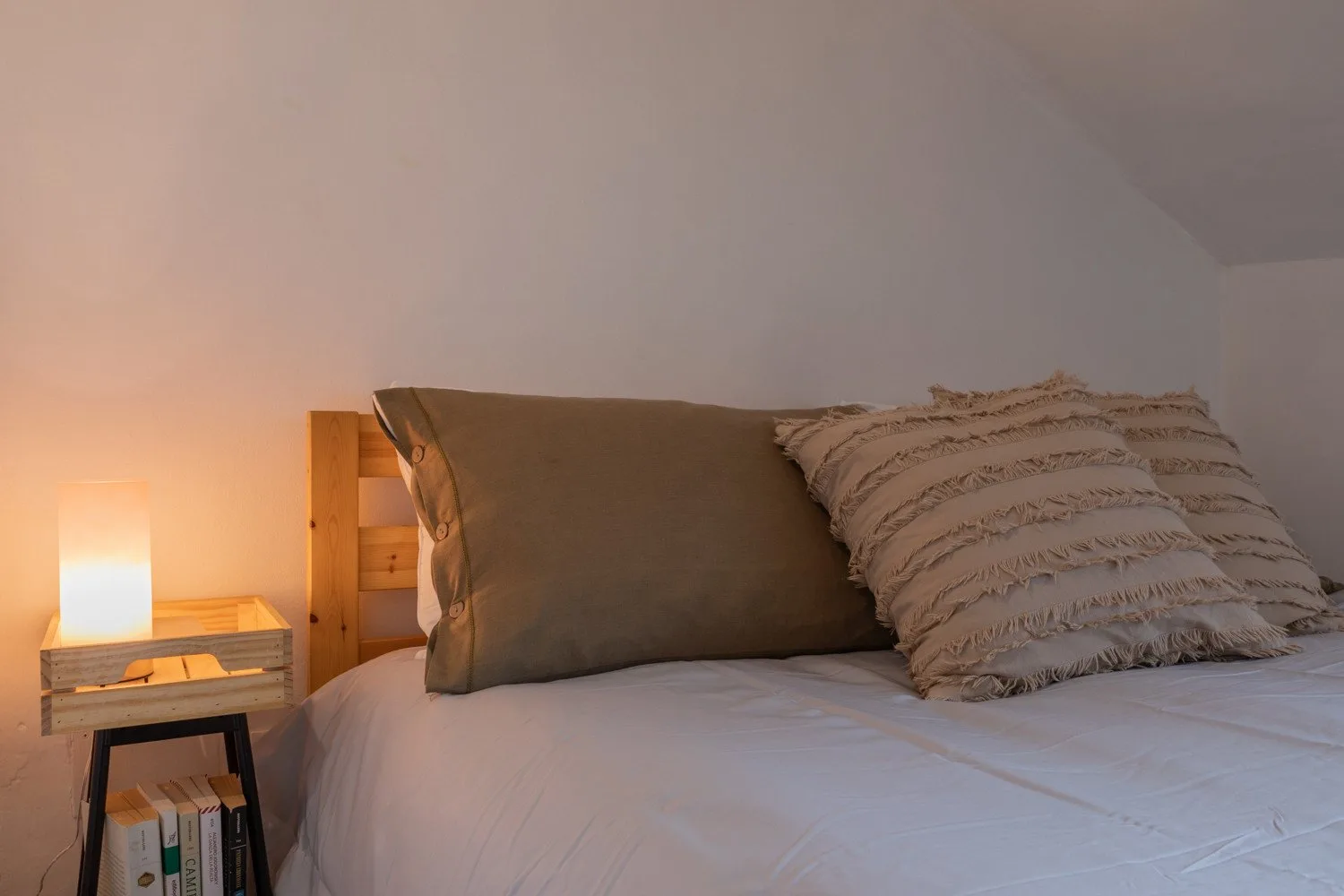 A bedroom with a neatly made bed and a warm bedside lamp.