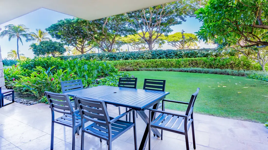 Una zona de comedor en el patio da a un césped verde y un jardín ajardinado.