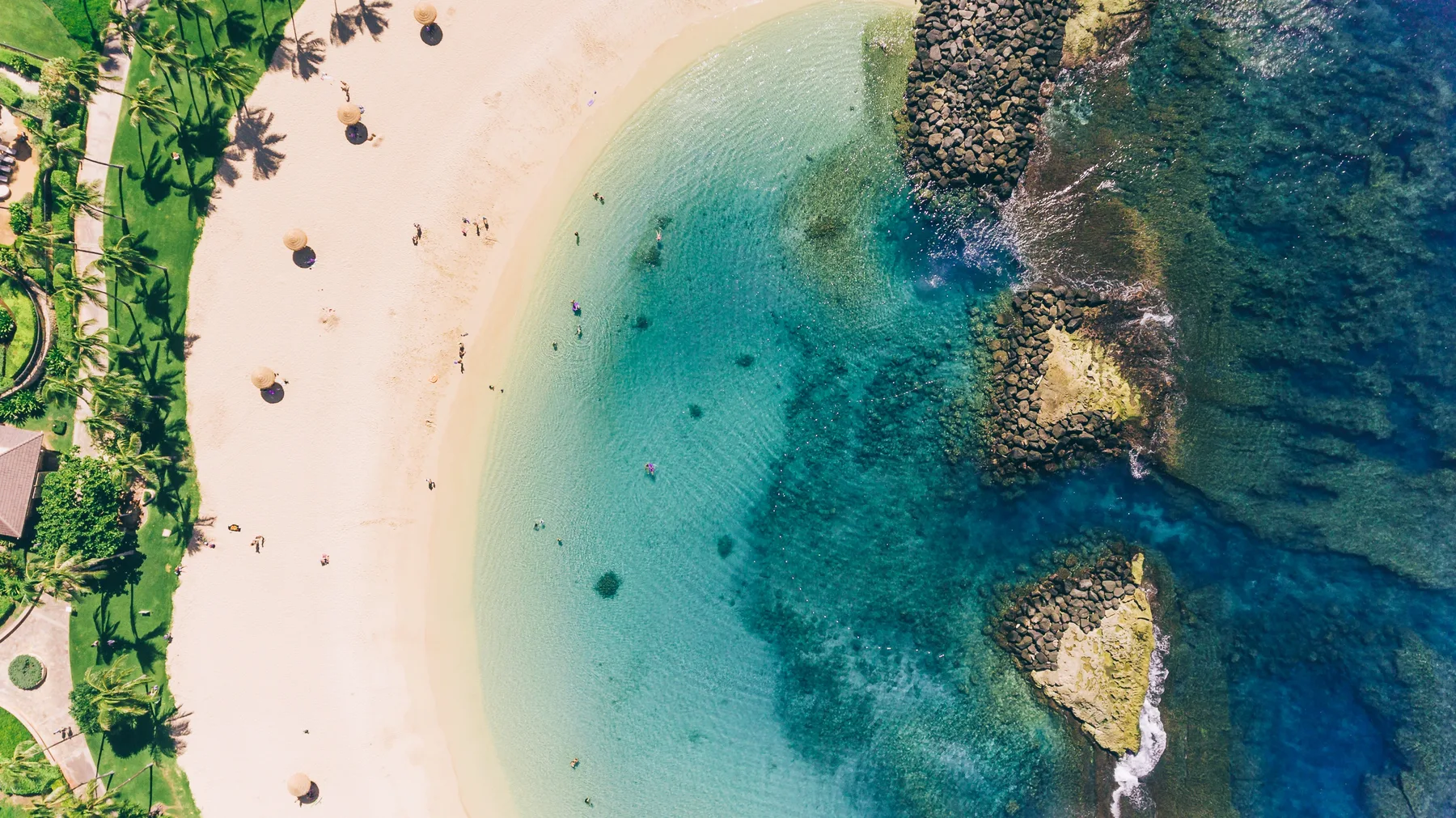 Vista aérea de una playa de arena junto a aguas turquesas y afloramientos rocosos.