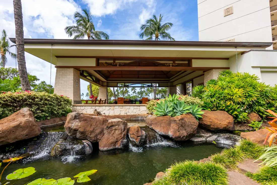 Una entrada exterior cubierta da a un estanque ajardinado con rocas y plantas tropicales.