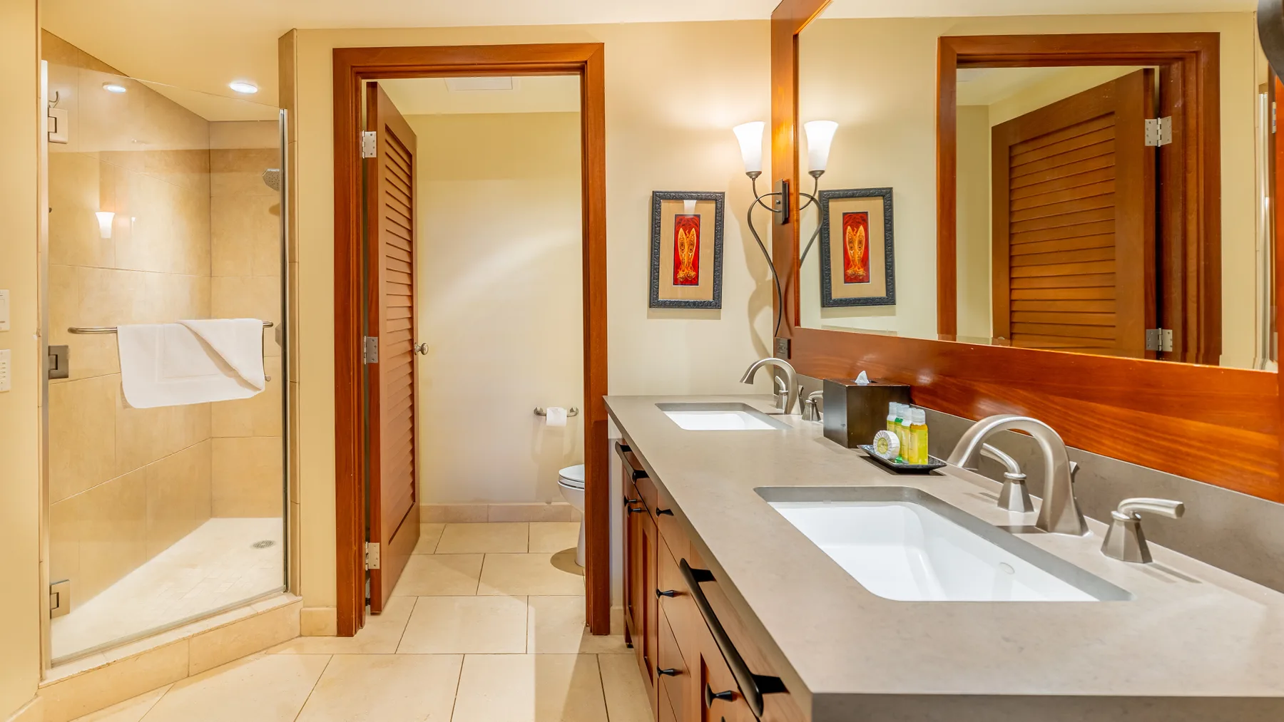 Un tocador de baño con dos lavabos da a un espejo grande, junto a una ducha de vidrio.
