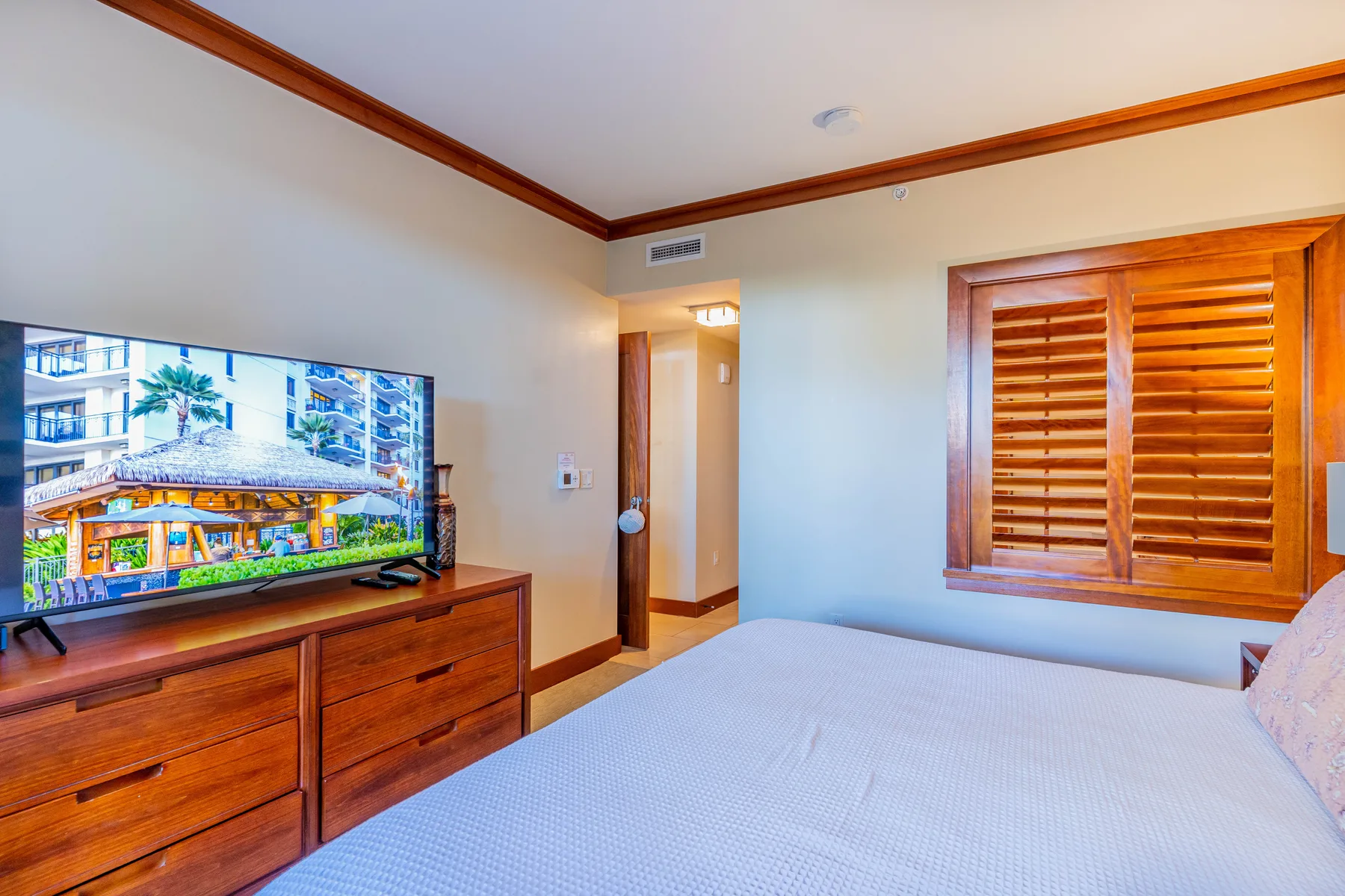 Un dormitorio con cama, televisor, cómoda de madera y ventana con persianas.
