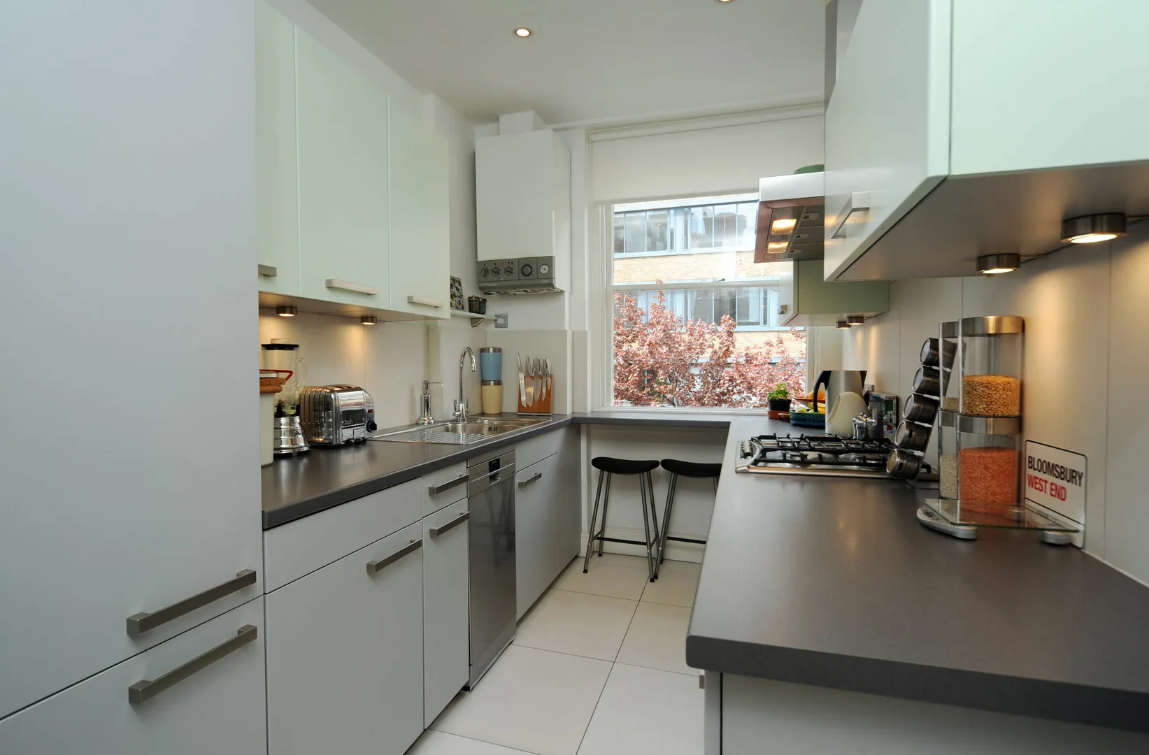 A modern kitchen with white cabinets, dark countertops, and a window above the sink.