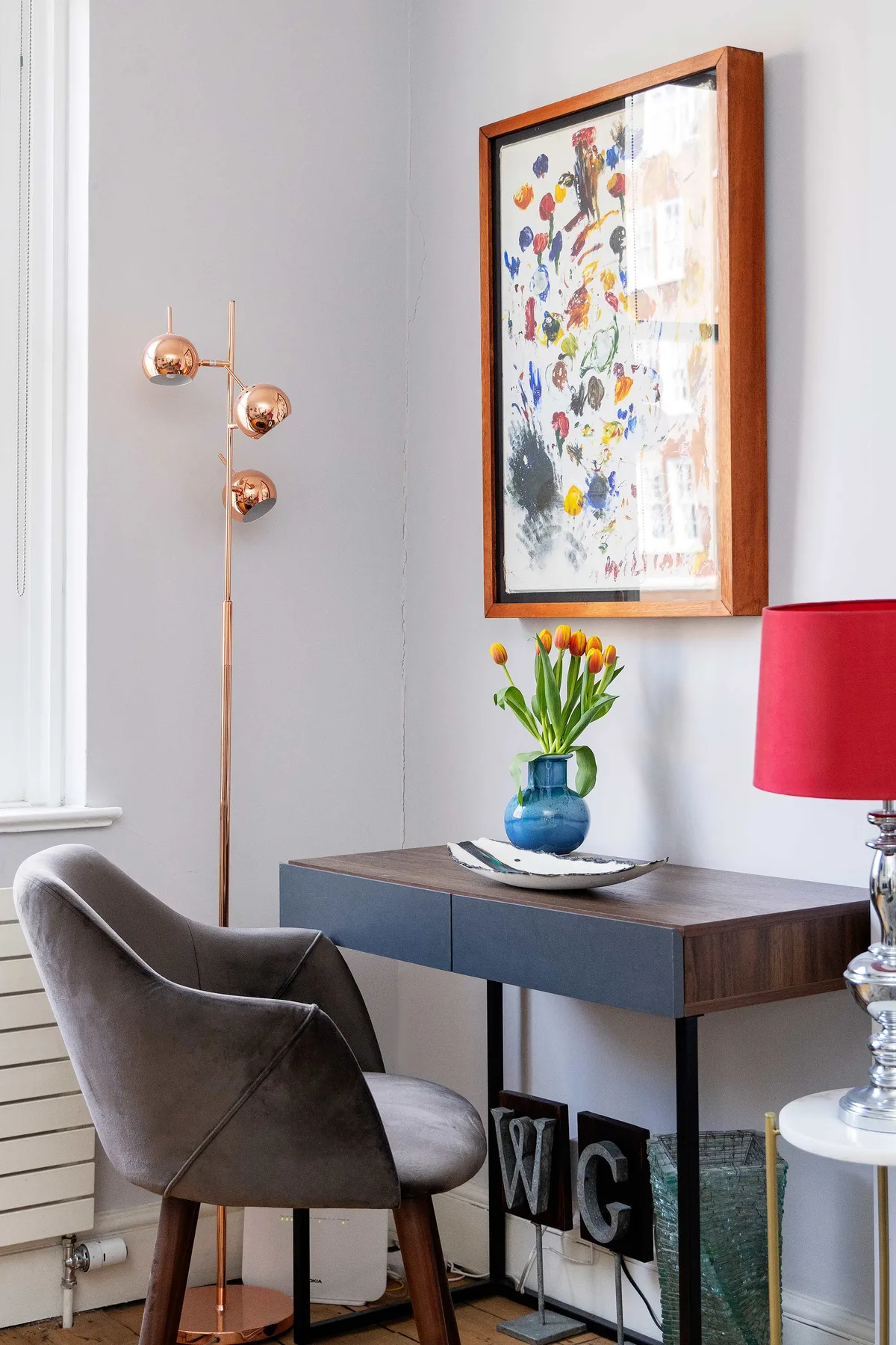 A sitting area with a gray chair, console table, and colorful framed artwork.