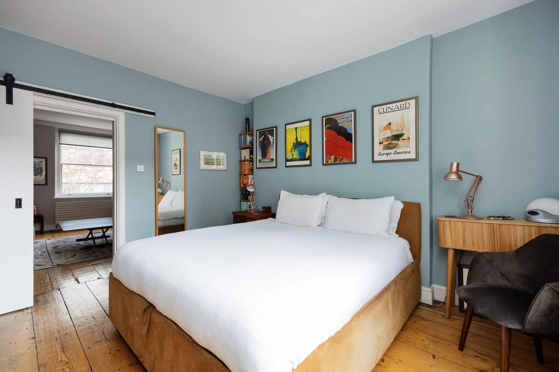 A bedroom with a large bed, framed artwork, and a desk.