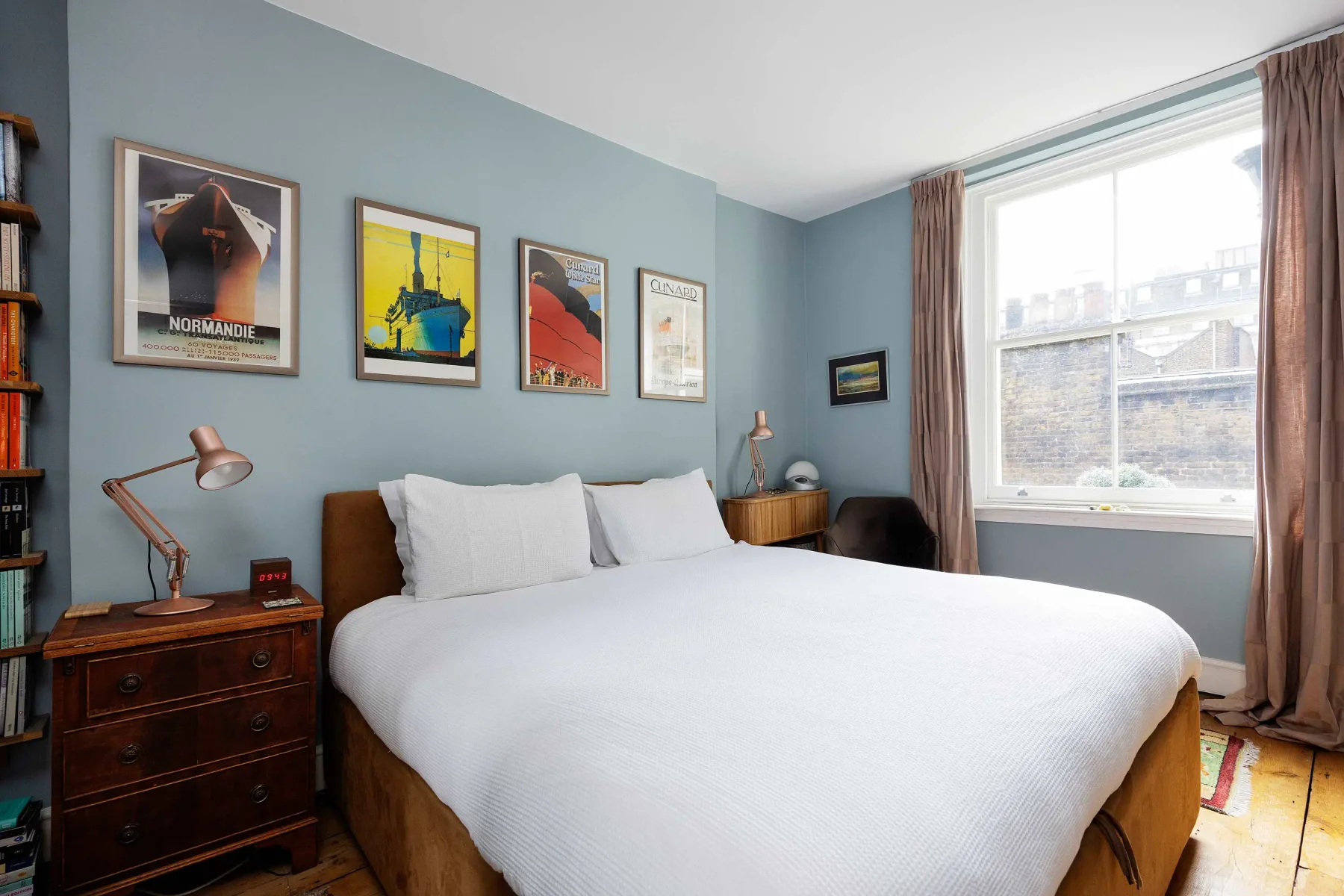A bedroom with a neatly made bed and framed posters on the wall.