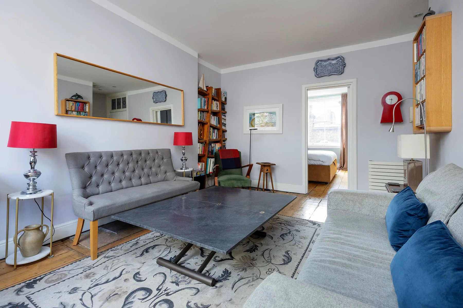 A living room with seating around a low table and a doorway to a bedroom.