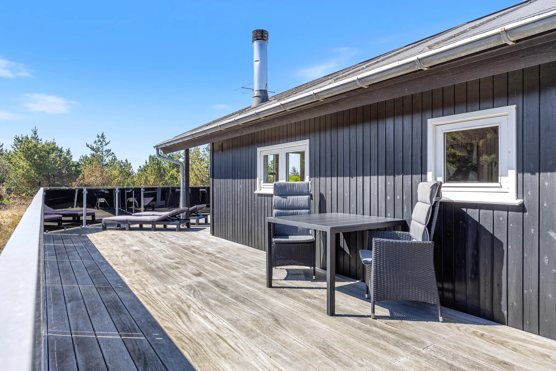 Una terraza de madera junto a una casa oscura, con una mesa y asientos.