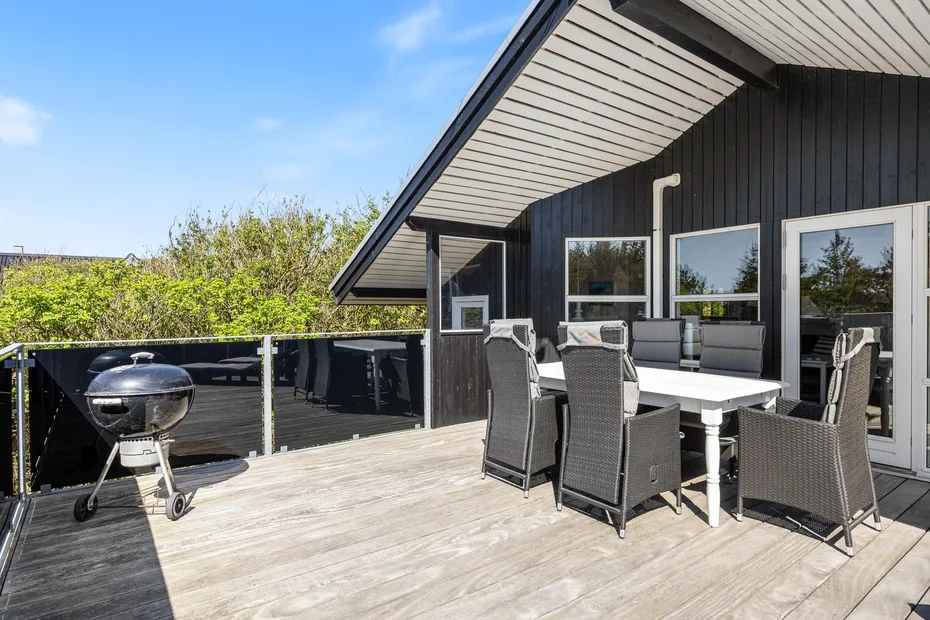 Una terraza exterior tiene una mesa de comedor y asientos junto a una parrilla.