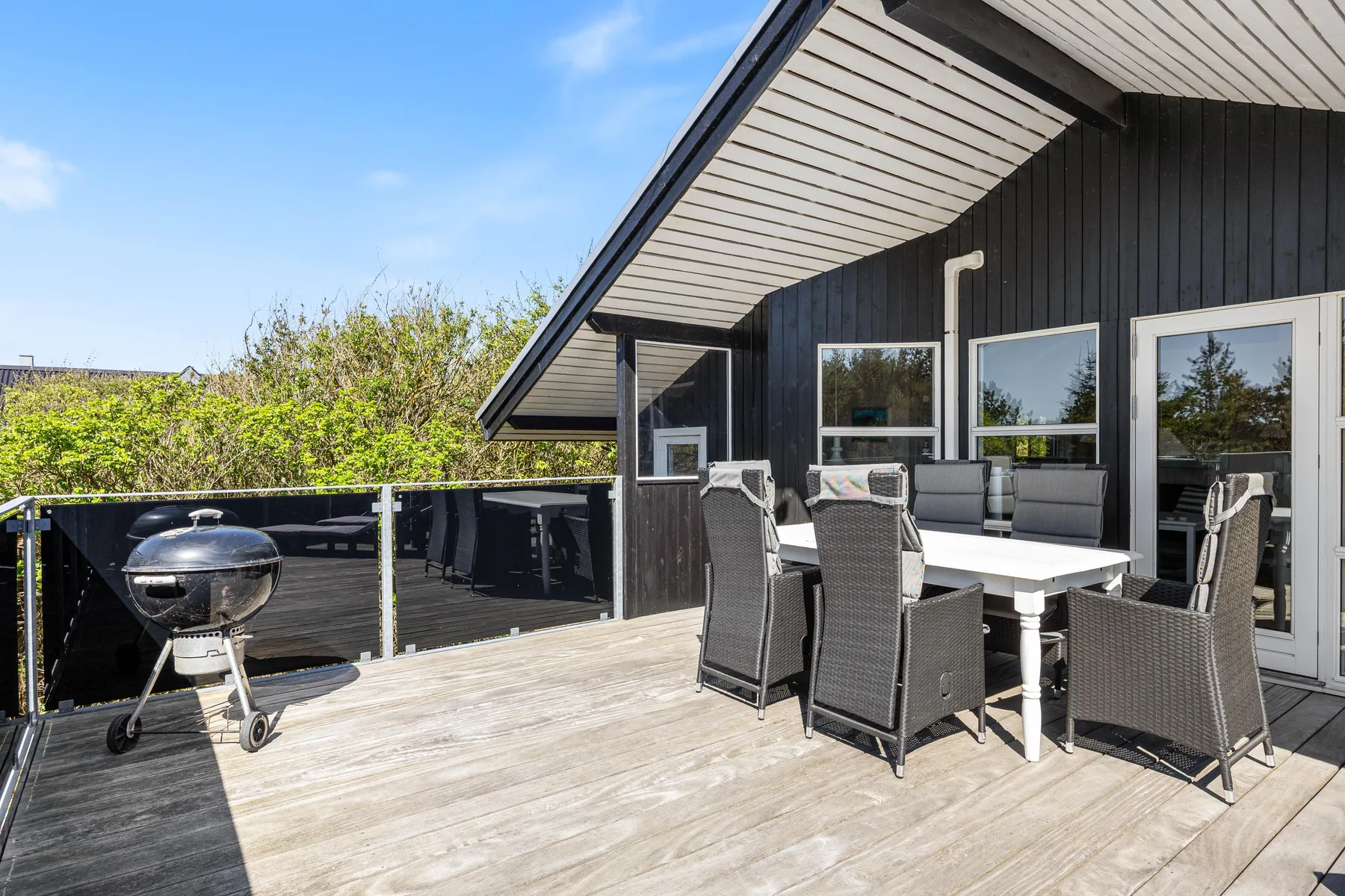 Una terraza exterior con mesa de comedor, asientos y una barbacoa junto a una casa oscura.