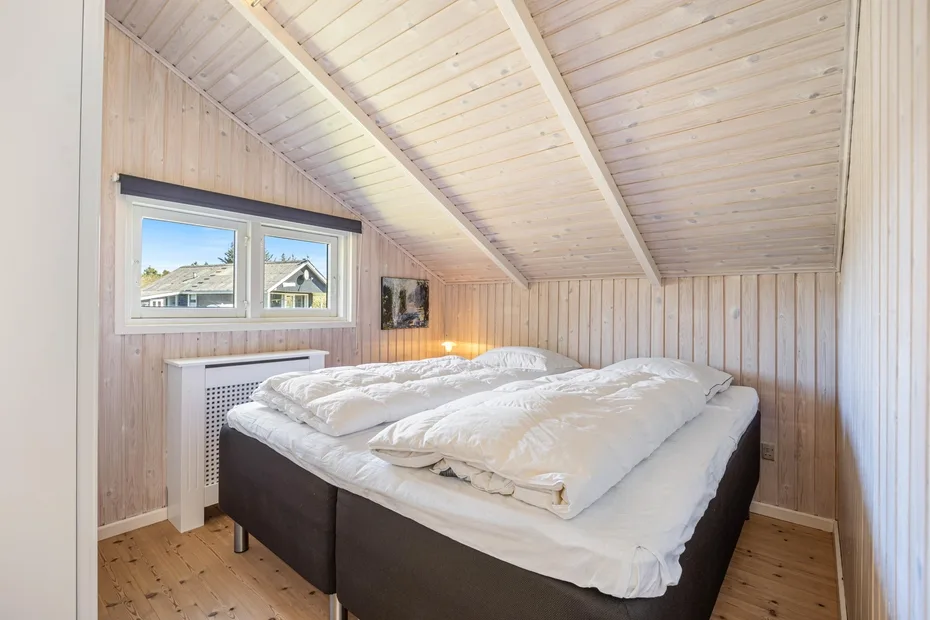 Un dormitorio con una cama bajo un techo inclinado revestido de madera.