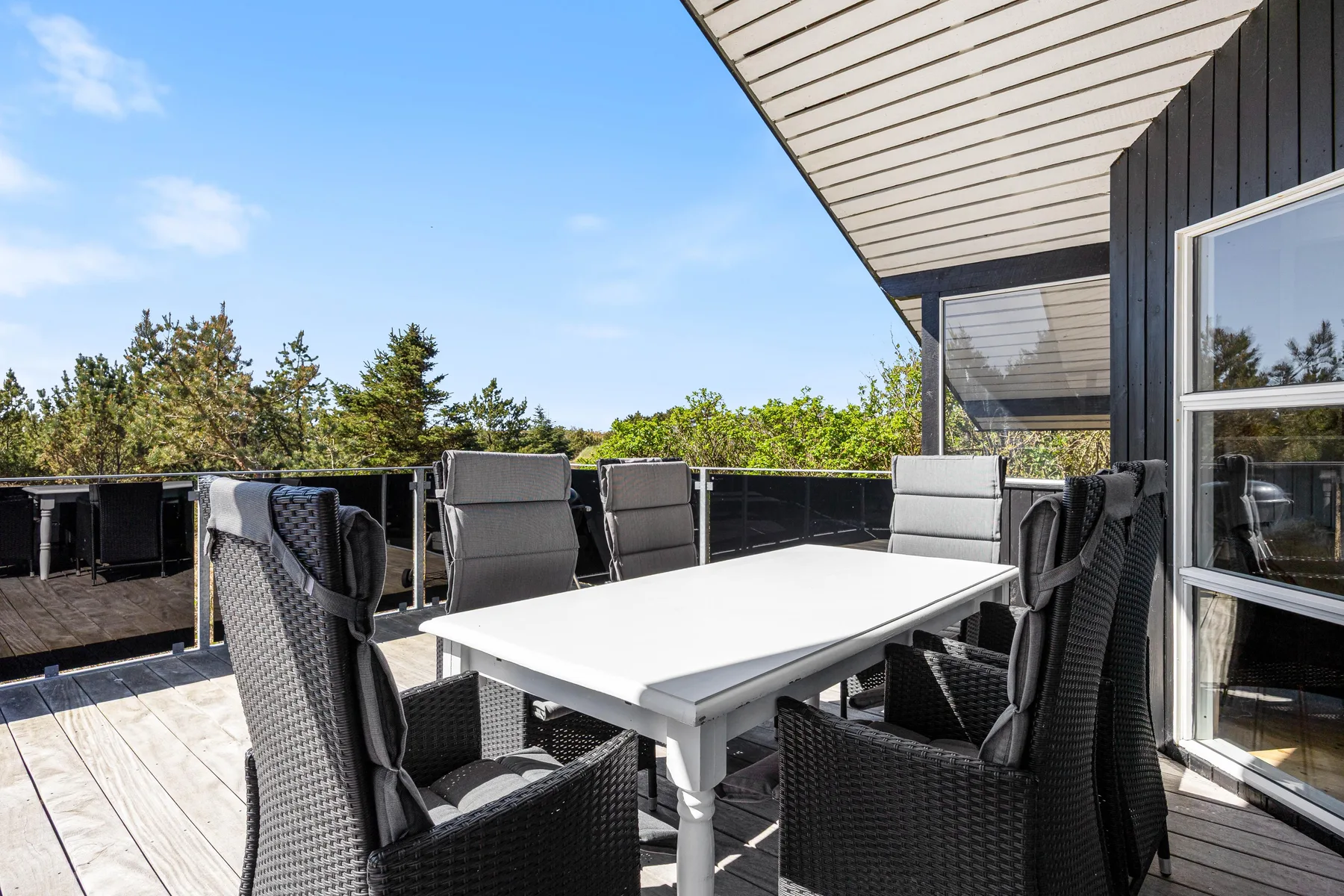 Una zona de comedor al aire libre con mesa y asientos en una terraza soleada.