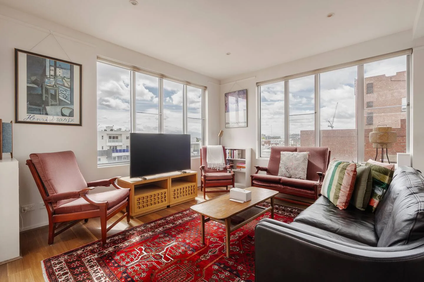 A bright living room with large windows, a television, and seating around a coffee table.