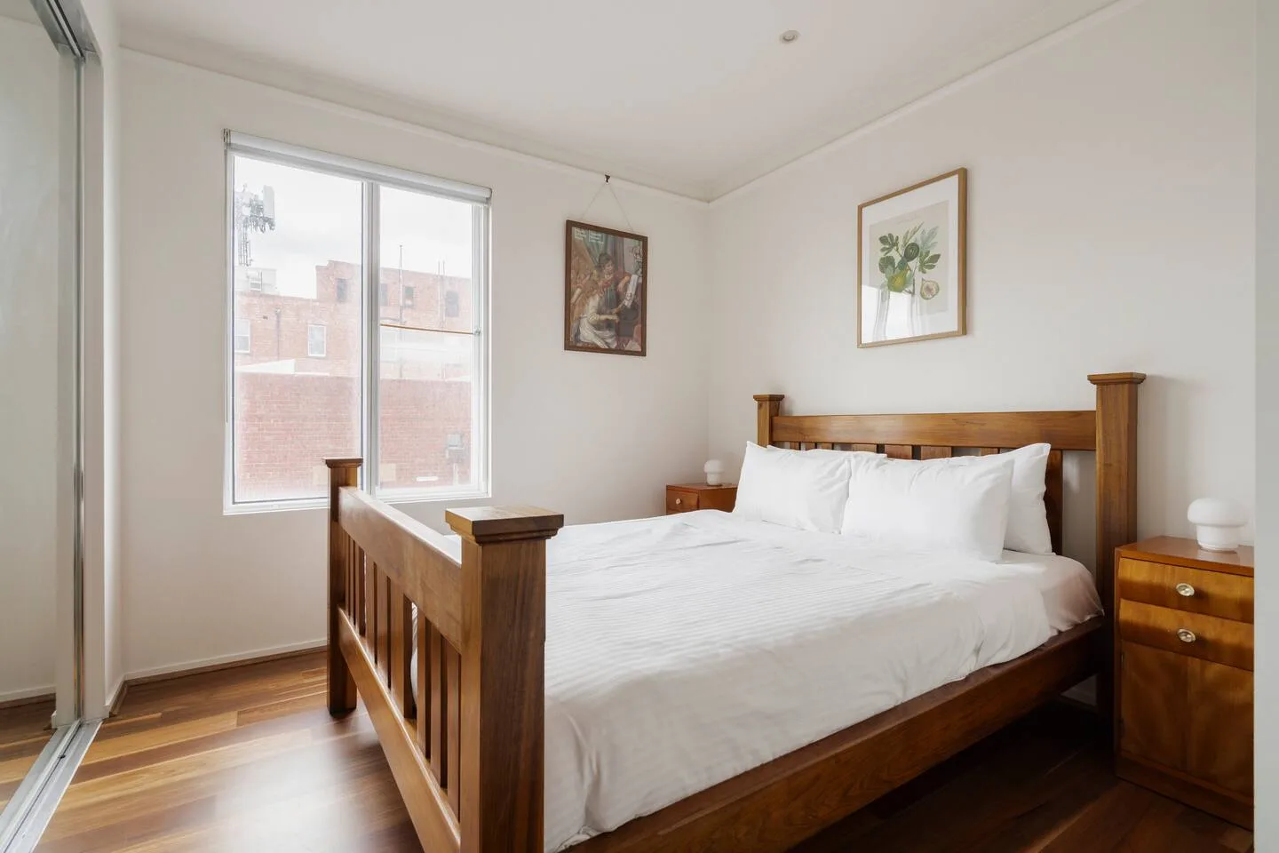 A bedroom with a wooden bed, white bedding, and a large window.
